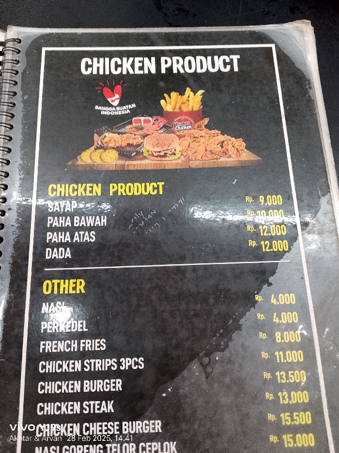 The image is a close-up of a menu board for a fast food restaurant in Patrol, Indonesia. The menu board is black and has yellow writing on it. The menu lists the following food items: Sayap, Paha Bawah, Paha Atas, Dada, Nasi, Perkedel, French Fries, Chicken Strips 3PCs, Chicken Burger, Chicken Steak, Chicken Cheese Burger, and Nasi Goreng Telor Ceplok. Each food item has its price in Indonesian Rupiah written beside it. The menu board also features a logo for the restaurant, which includes the words "Bangga Buatan Indonesia" and "The Best Chicken." The menu board is attached to a wall. The environment appears to be a restaurant, but it is unclear if it is a sit-down restaurant or a take-out restaurant. The coordinates provided place the restaurant in Patrol, Indonesia, but the image does not provide any further information about the restaurant's location. The image was taken with a smartphone camera, and the camera appears to be slightly angled, making the menu board look slightly distorted. The image was taken in a dimly lit environment, and the surface of the menu board has a slight sheen from the reflection of the light. The menu board also appears to have some minor water damage.