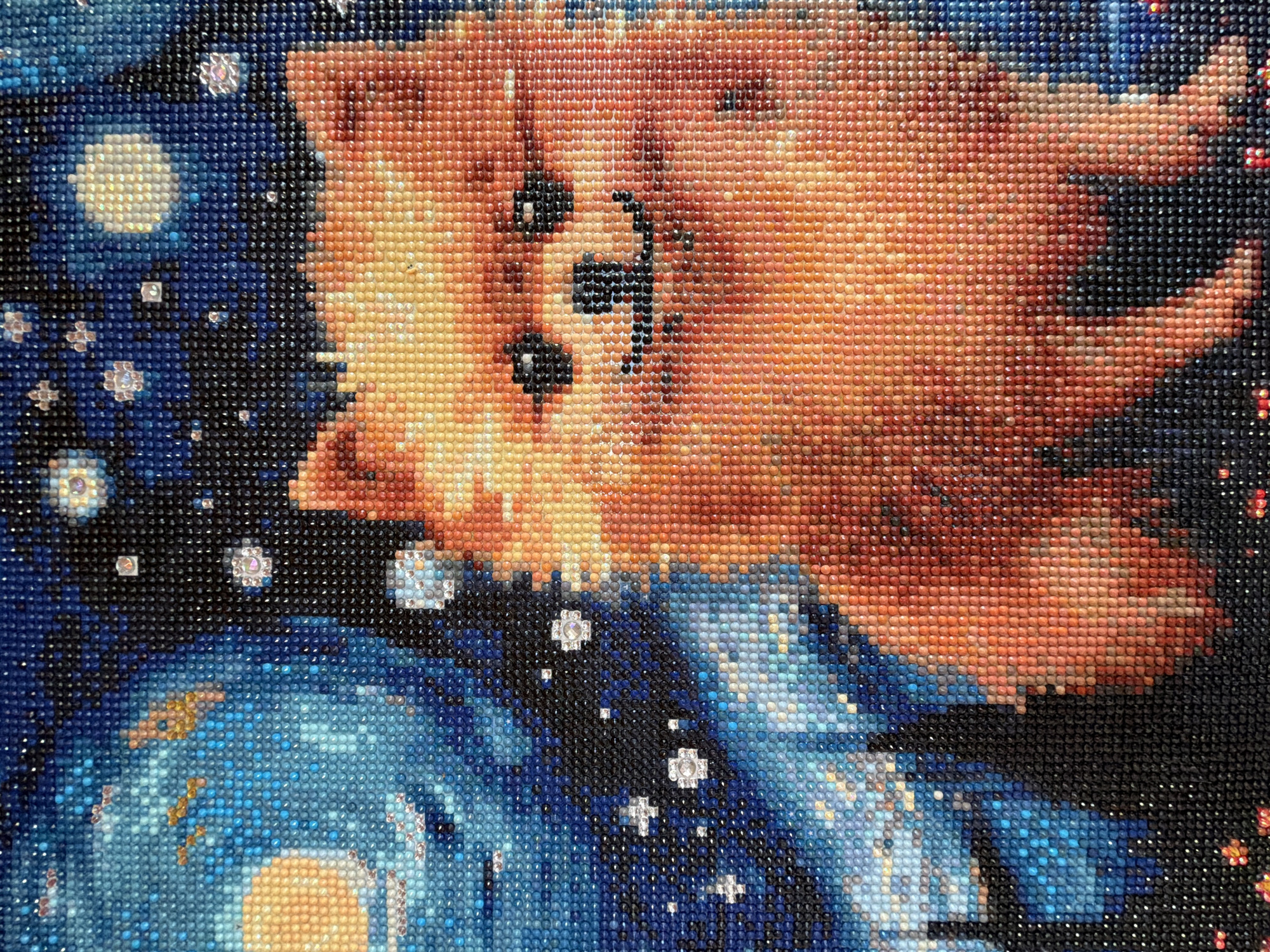 A close-up image of a diamond painting depicting a dog on a starry night background. The dog, rendered in orange, yellow, and brown tones, is positioned on the upper right of the frame, its face clearly visible with black details for eyes, nose, and mouth. The background mimics Vincent van Gogh's "The Starry Night," with swirling patterns of blue, black, and white to represent the night sky, complete with prominent stars and a crescent moon. The painting is made up of many small, colorful, individual diamond pieces.