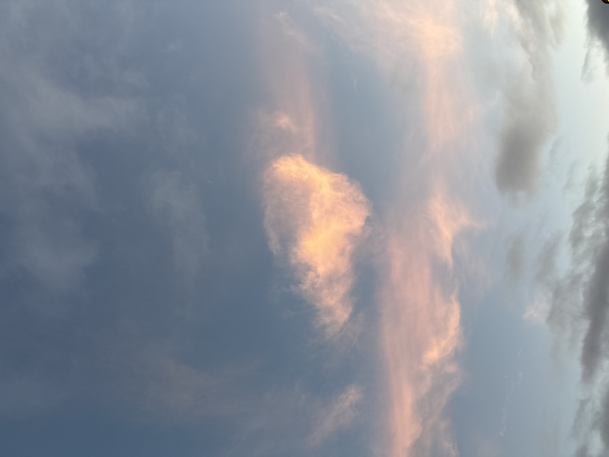 The image shows a cloudy sky at what appears to be sunset, with streaks of pink and orange light illuminating some of the clouds. The sky is a blend of blue and pale grey. The clouds are wispy and scattered. The scene appears to be an outdoor view, possibly a landscape or seascape, though no specific landmarks are visible. Given the prompt's reference to Tramore, Ireland, this could be a view of the sky over the town or its coastline. No people or specific objects are discernible in the frame.