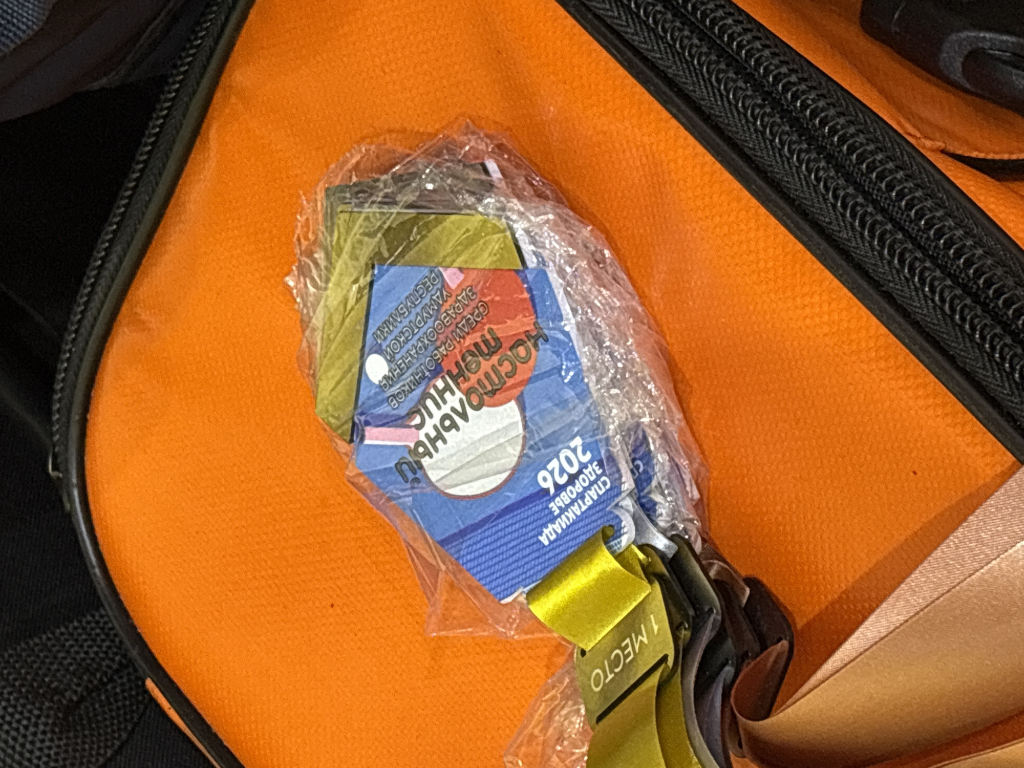 The image shows several awards and medals, still in their packaging, lying on top of an orange bag. The text on one of the awards reads "Спартакиада Здоровье 2026", and a yellow ribbon attached to one of the medals reads "1 место", indicating first place. The location of the image is Izhevsk, Russia.