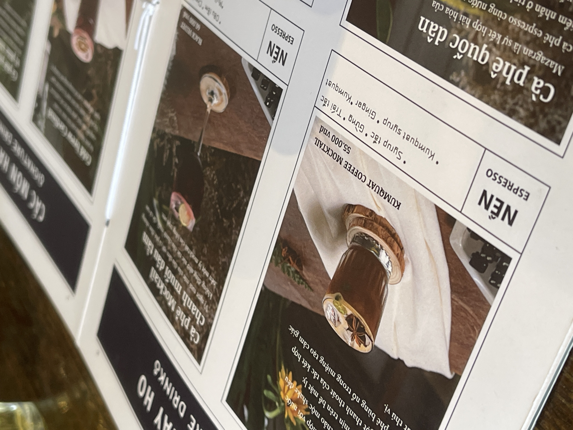 The image shows a section of a menu in what appears to be a cafe or restaurant, likely located in Da Lat, Vietnam. The menu features descriptions and images of various drinks, including coffee and mocktails. Visible menu items include "Cà phê Mocktail chanh muối dâu tầm," "KUMQUAT COFFEE MOCKTAIL," and "Cà phê quốc dân." Prices are listed in Vietnamese Dong (vnd). The menu design is modern, with a mix of text and imagery. The image suggests a focus on local and unique beverages.