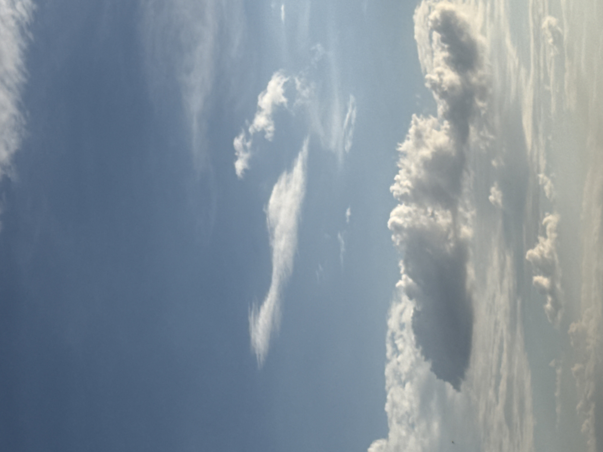 The image depicts a sky with scattered clouds, appearing to be taken from an elevated perspective, possibly a rooftop or a hilltop. The clouds are varied in size and texture, with some appearing thin and wispy, while others are more dense and puffy. The sky is a light blue, suggesting it is daytime, likely mid-morning or afternoon. There are no discernible landmarks or structures that would immediately place the scene within Abovyan, Armenia. The image is solely focused on the atmospheric conditions.