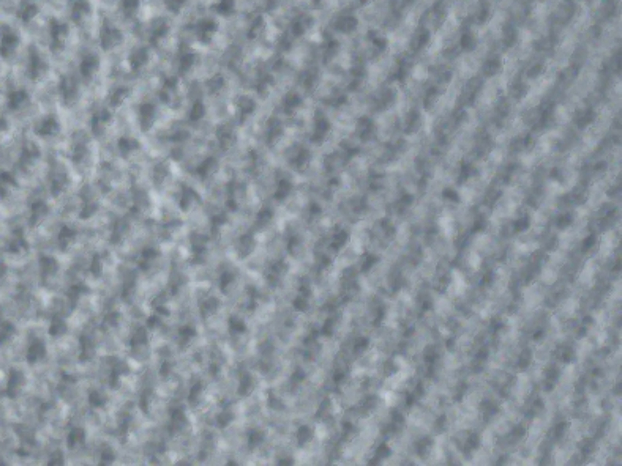 The image is a close-up, abstract view of a textured surface, likely fabric or a similar material. It is predominantly gray with subtle variations in tone and hints of lighter and darker shades that create a sense of depth and pattern. The texture appears to be woven or knitted, with a repeating diagonal pattern of raised and recessed areas. There are no discernible objects, people, or environmental features visible. The image does not contain any information that would allow for its location to be determined in Varna, Bulgaria.