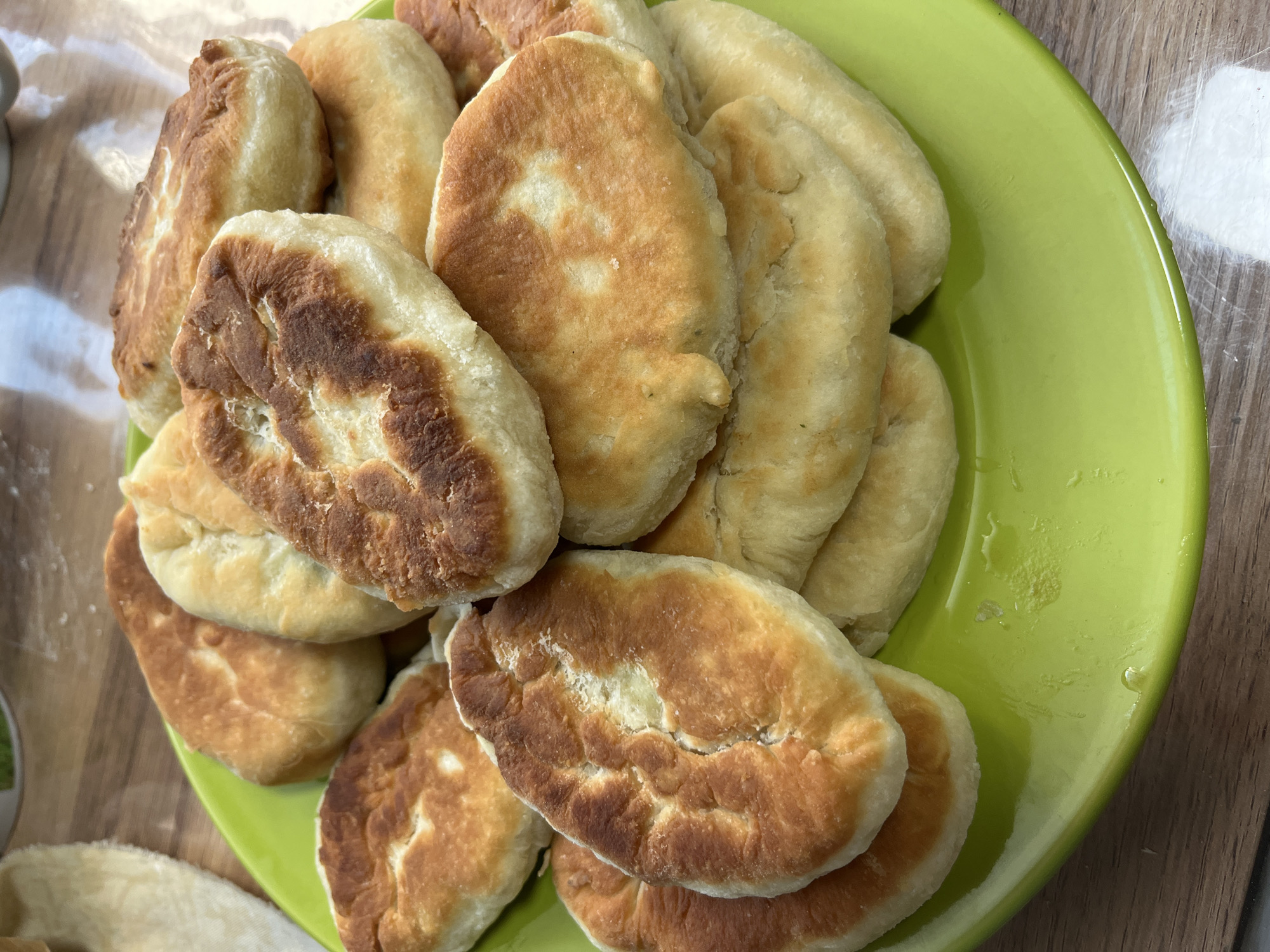 A plate of fried pastries is pictured on a wooden table. The pastries are golden brown and appear to be filled. The plate is green and has some liquid on it.