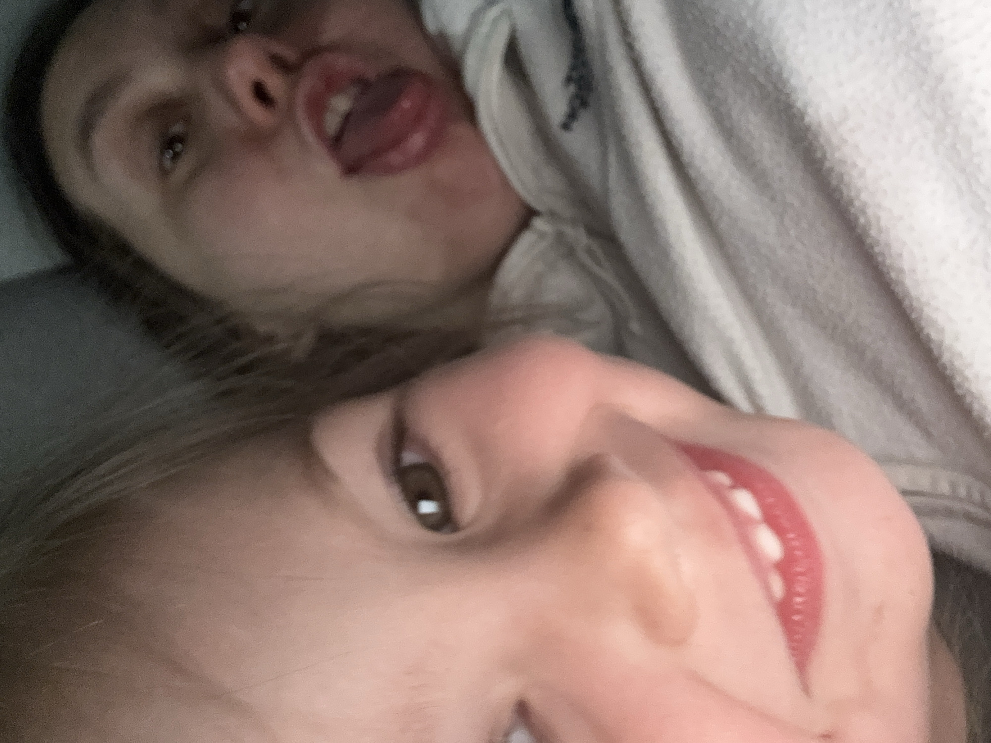 The image shows two individuals in a close-up selfie. The person in the foreground is a child with light skin, light-colored hair, and visible teeth. The person in the background appears to be an adult, with darker hair, sticking their tongue out. They are possibly wearing a light-colored hoodie. The image does not contain information relating to Zelenogradsk, Russia.