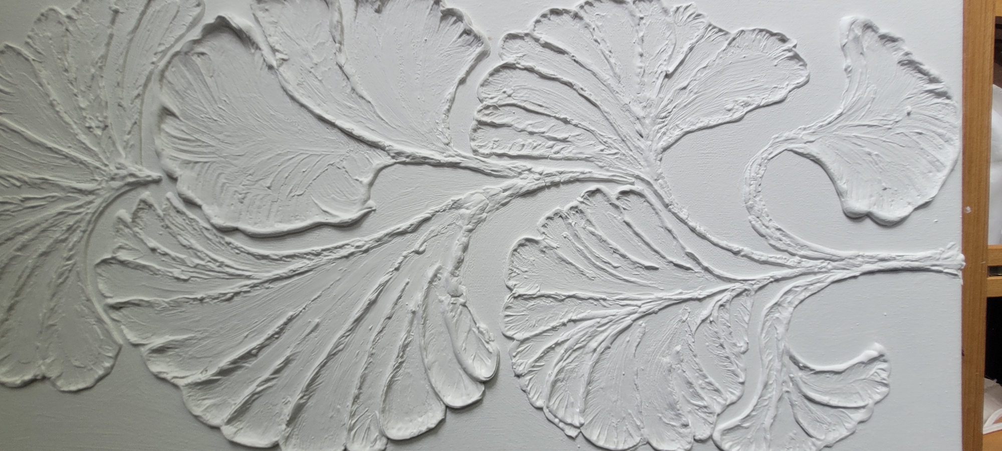 The image displays a close-up, top-down view of a white, textured artwork featuring a stylized branch with multiple ginkgo leaves. The leaves are rendered in relief, with distinct veins and a slightly rough, impasto surface. The composition is abstract, focusing solely on the form and texture of the botanical elements against a plain white background. No specific location in Montreal, Canada, is identifiable within the image. The image appears to be a photograph of a piece of art, possibly a sculpture or a textured painting.