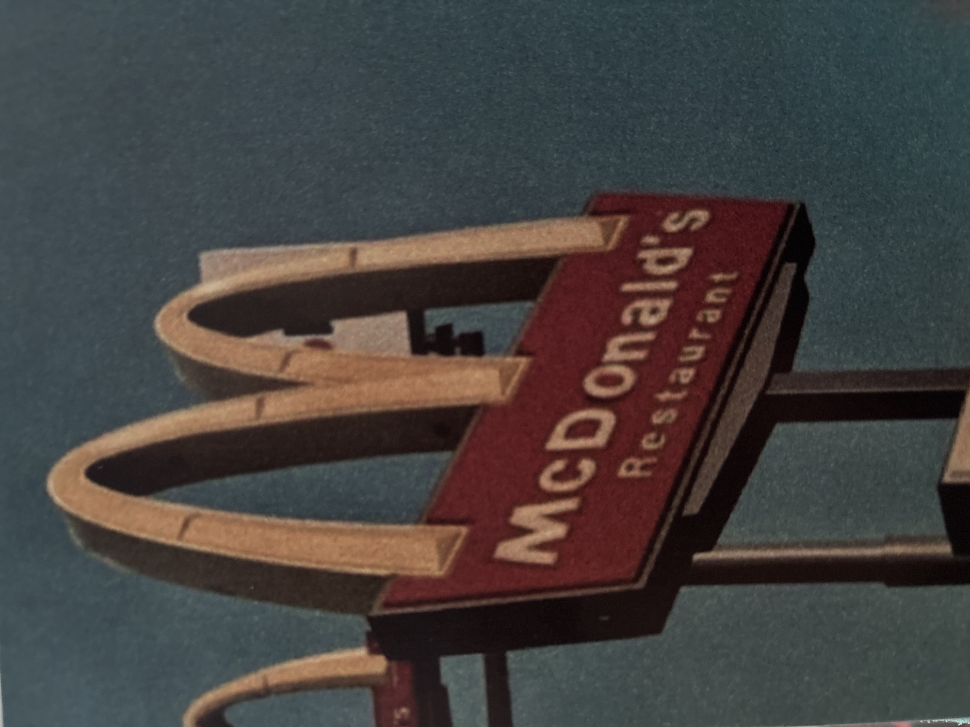 The image shows a McDonald's restaurant sign with the iconic golden arches and a rectangular sign reading "McDonald's Restaurant" in red letters. The background is a blurry blue-grey color, suggesting the sky. There is no indication in the image itself to determine if this is specifically in Votkinsk, Russia.