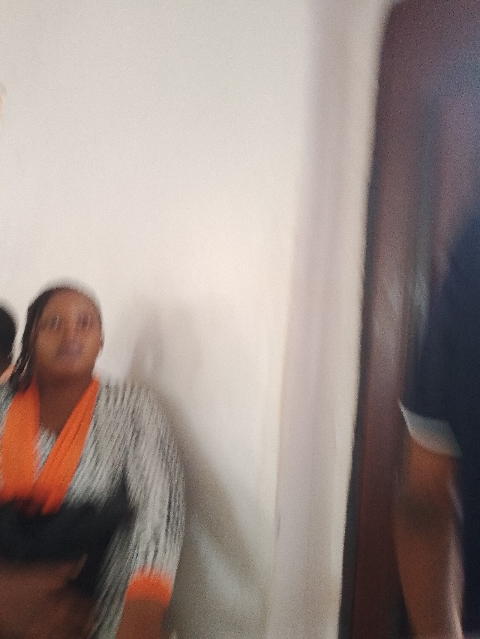 A woman in a striped top with orange trim is standing inside. She appears to be in a room in a building or house. The location is stated as OGBOKO, Nigeria.