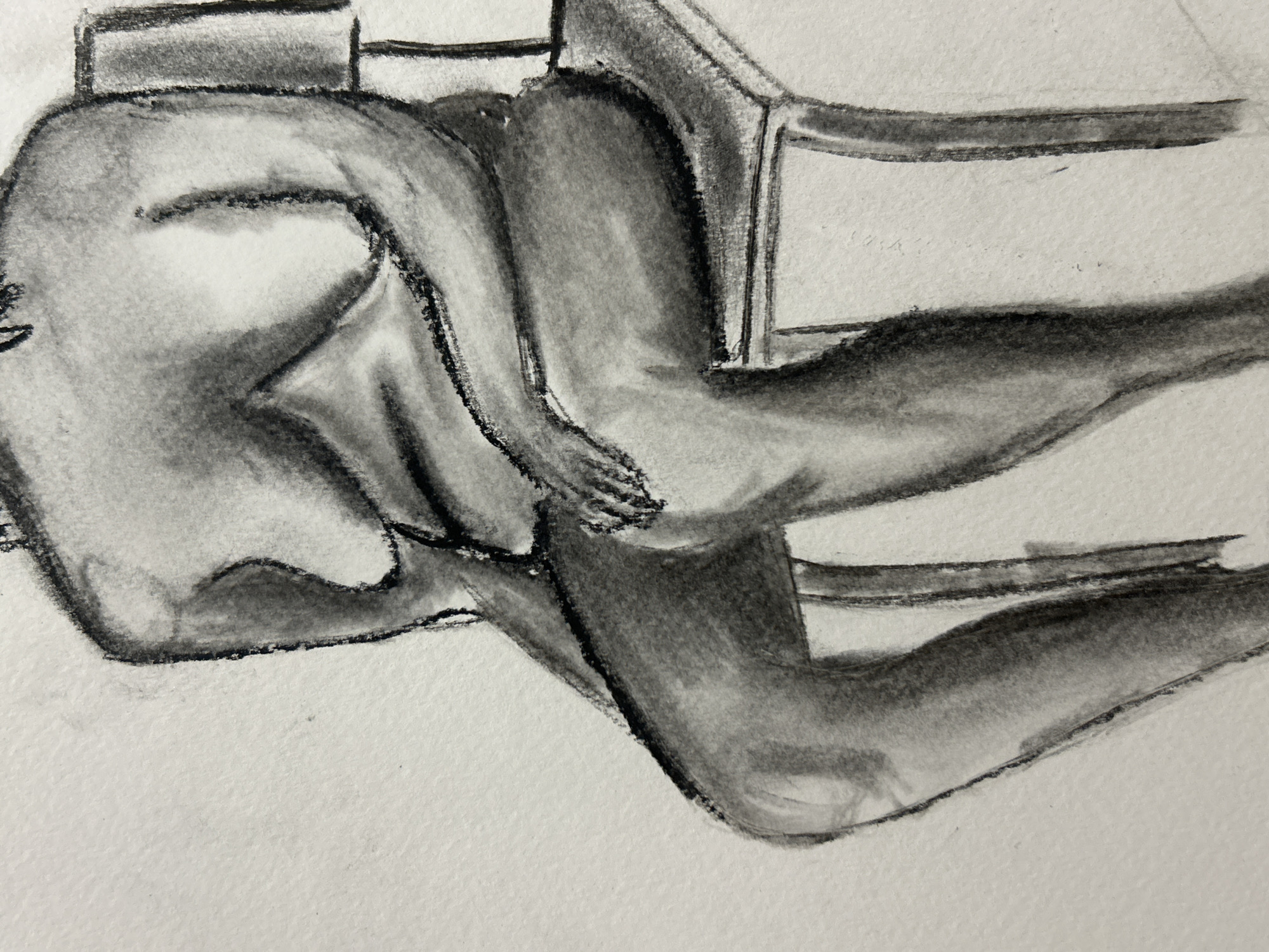 A charcoal drawing depicts a nude figure seated in a chair. The figure is facing away from the viewer, with their head turned slightly to the left. The figure's arms are resting on their legs, and their hands are clasped together. The chair is simple in design and appears to be made of wood. The background is plain and white.
I cannot provide the specific location in Sofia, Bulgaria because the image does not contain any such indicators.