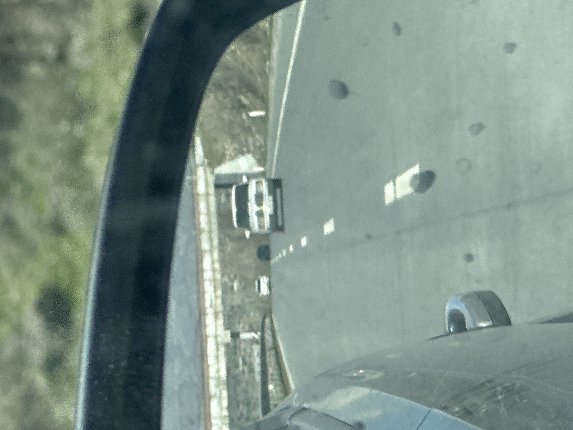The image is taken from inside a vehicle, possibly a car, looking out the window. A road runs parallel to a railway track. A white truck is on the road. Trees and greenery are visible on the left side of the frame. The location is unknown, as the city and place are unspecified.