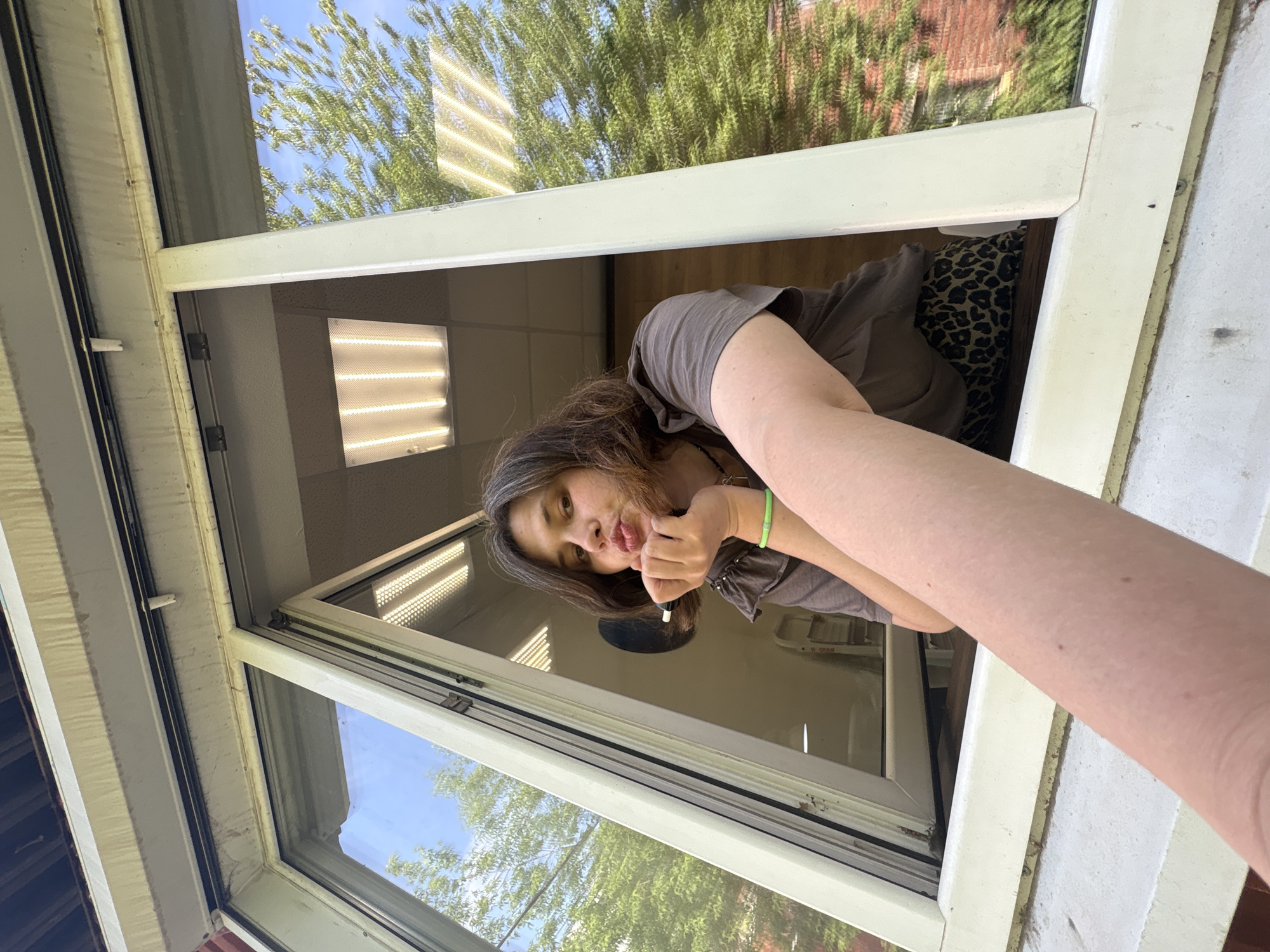 A woman leans out of an open window. The interior is an office setting with fluorescent lighting. The exterior shows trees and sky. The city of Chaikovsky, Russia, cannot be confirmed based on the image.