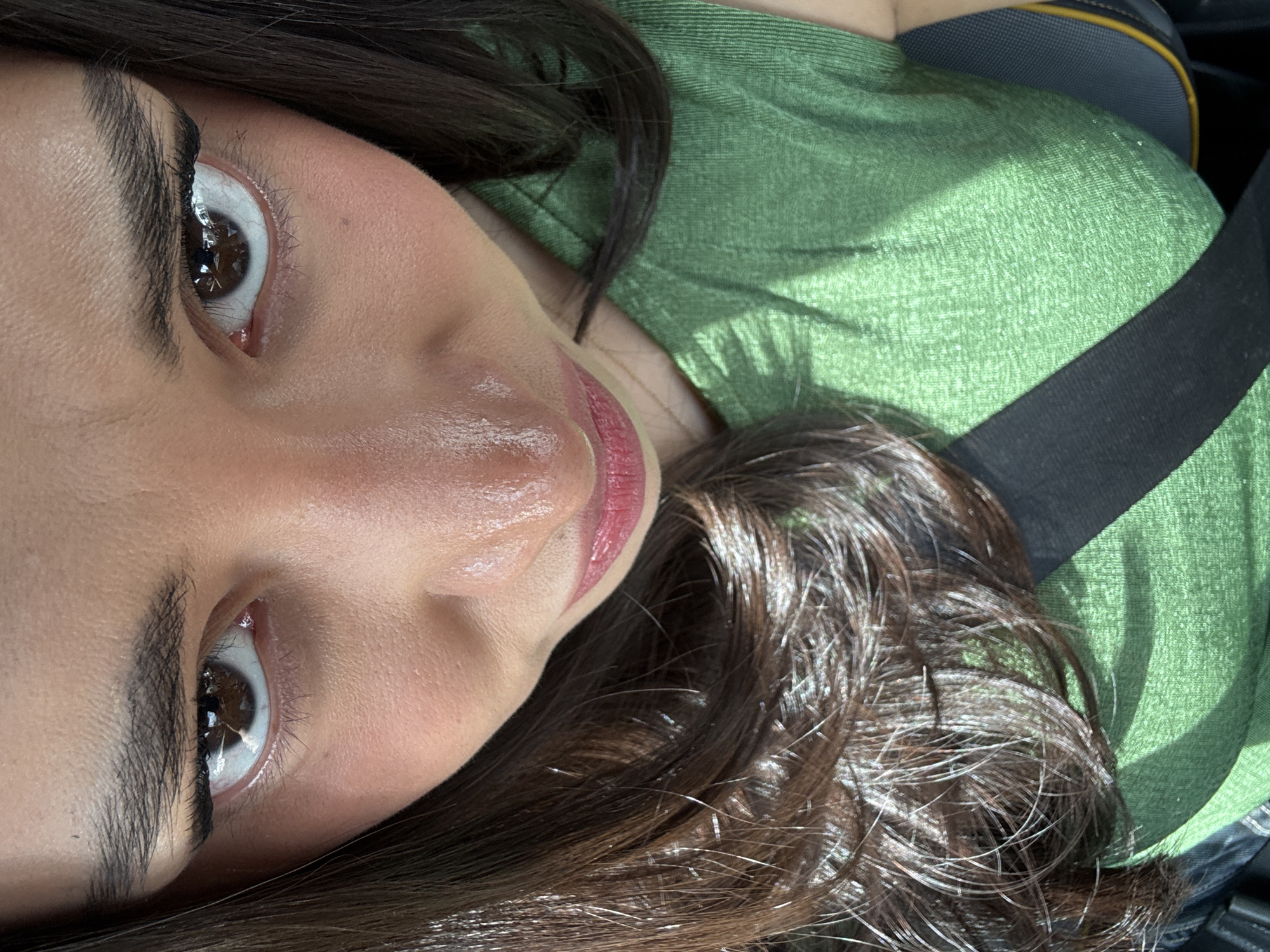 A close-up, angled perspective depicts a woman with brown hair and fair skin, wearing a green shirt and a black seatbelt. Her head is slightly tilted towards the camera. Her eyes are brown and she has full eyebrows. The background is indistinct, suggesting an interior setting. The image was taken inside a car, as suggested by the seatbelt. There is no indication that the photograph was taken in the city of Puebla, Mexico.