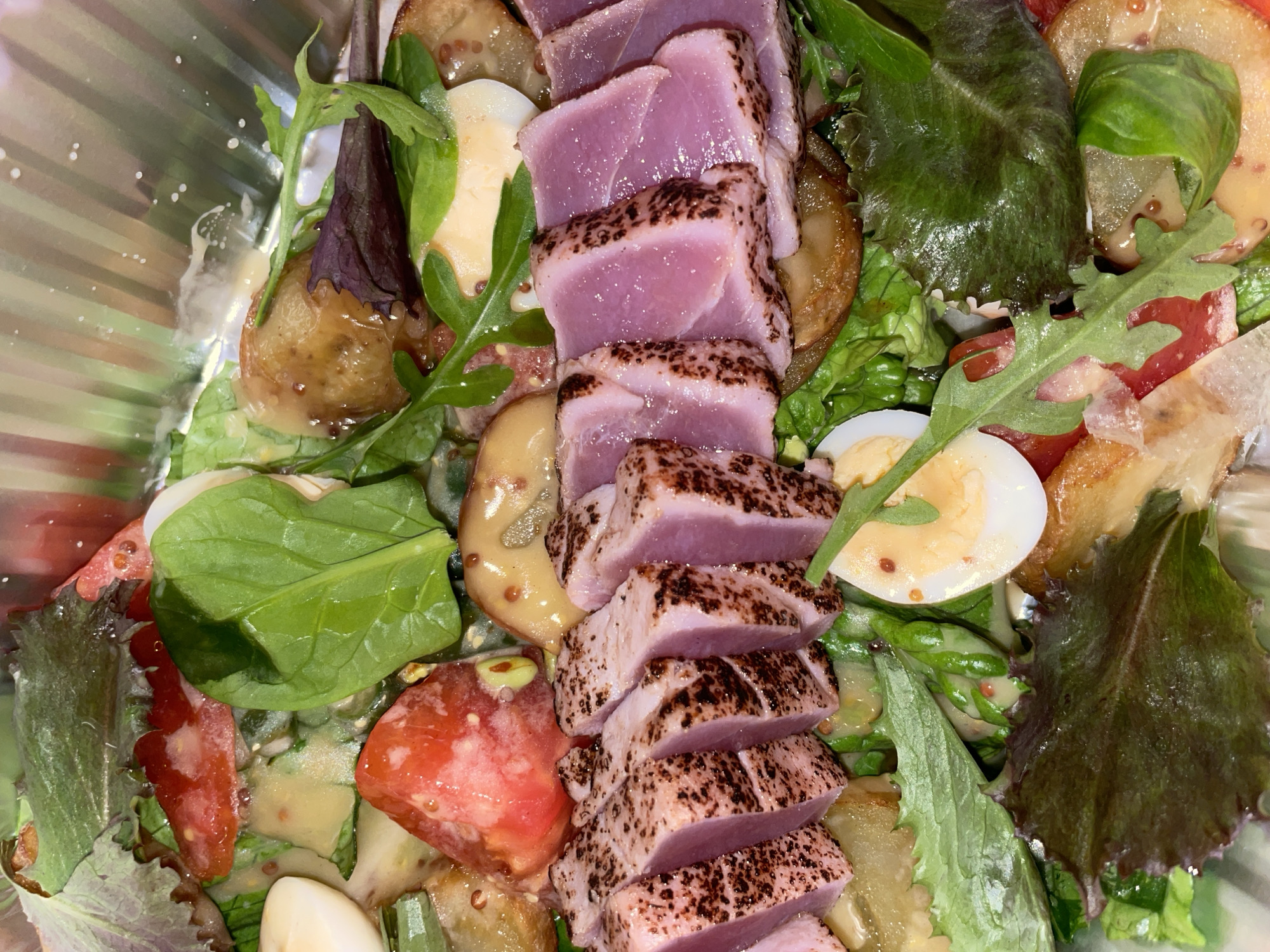 The image shows a salad in a clear bowl, likely served in a restaurant or home setting in Boreti, Montenegro. The salad features seared tuna steak, sliced and arranged in a row, alongside mixed greens, quartered quail eggs, sliced tomatoes, grilled eggplant, and what appears to be a vinaigrette dressing. The bowl is partially visible, and the ingredients are fresh and colorful, suggesting a Mediterranean-inspired dish.