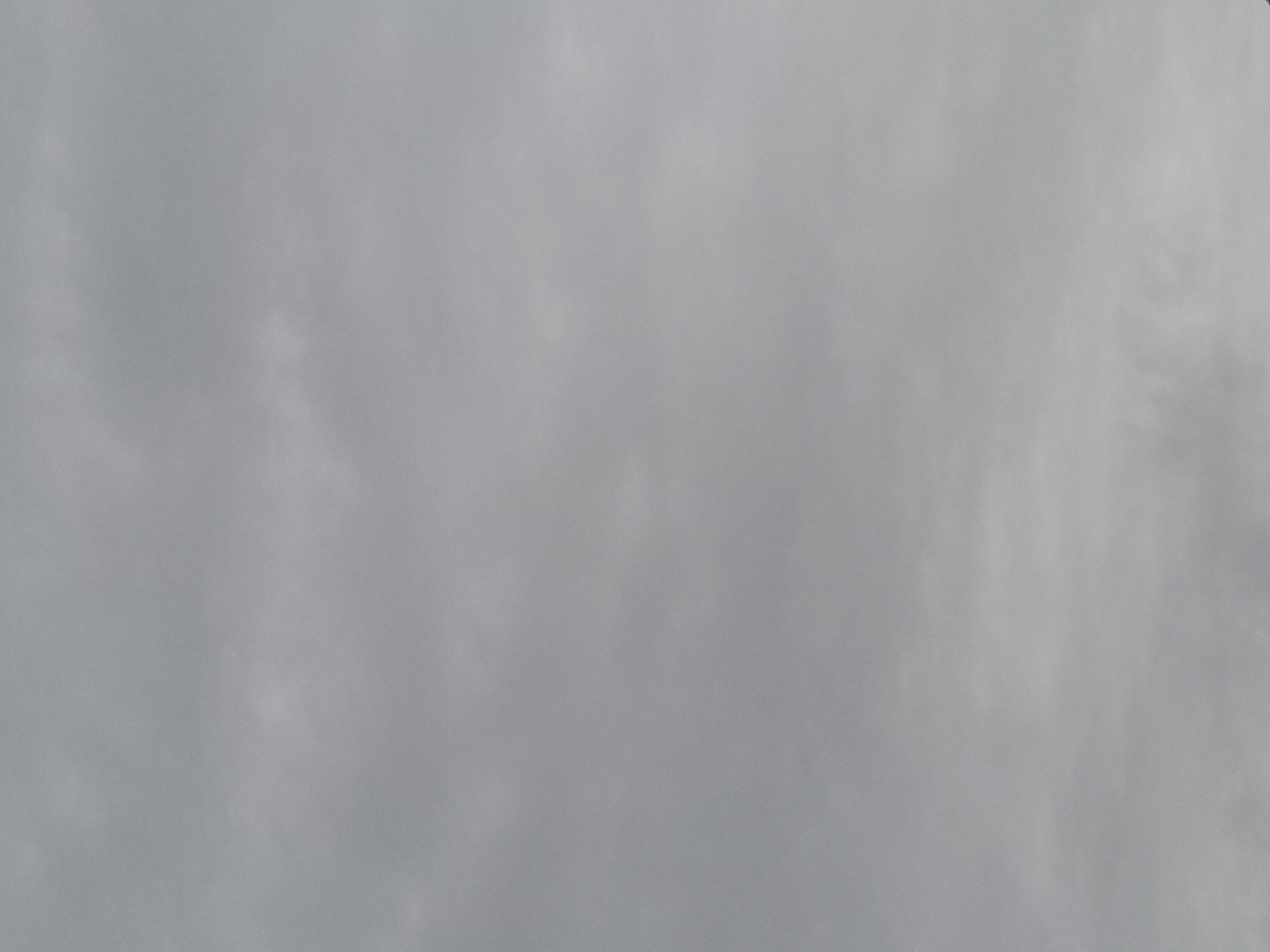 The image shows a gray, overcast sky. There is no indication of location or city present in the image. There are no people, subjects, objects, actions, or interactions visible. The environment consists solely of cloud cover.