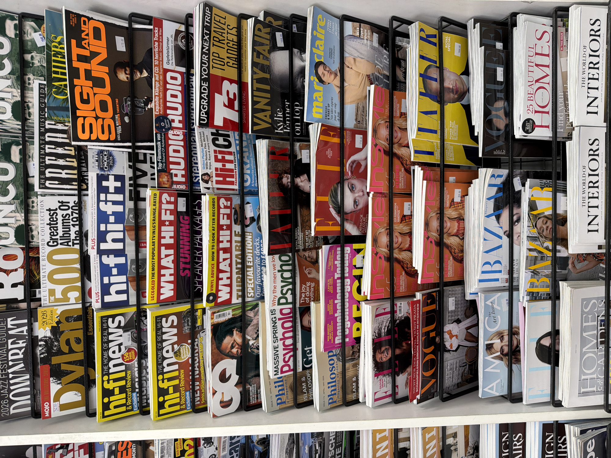 The image shows a magazine rack filled with various titles. The magazines cover a range of topics including music (e.g., "Sound and Sight", "Hi-Fi News"), fashion and lifestyle (e.g., "Vanity Fair", "Marie Claire", "Vogue"), and home decor ("Homes & Gardens", "The World of Interiors"). The magazines are arranged in a metal rack, suggesting a retail environment. The specific location in Belgrade, Serbia is not discernible from the image.