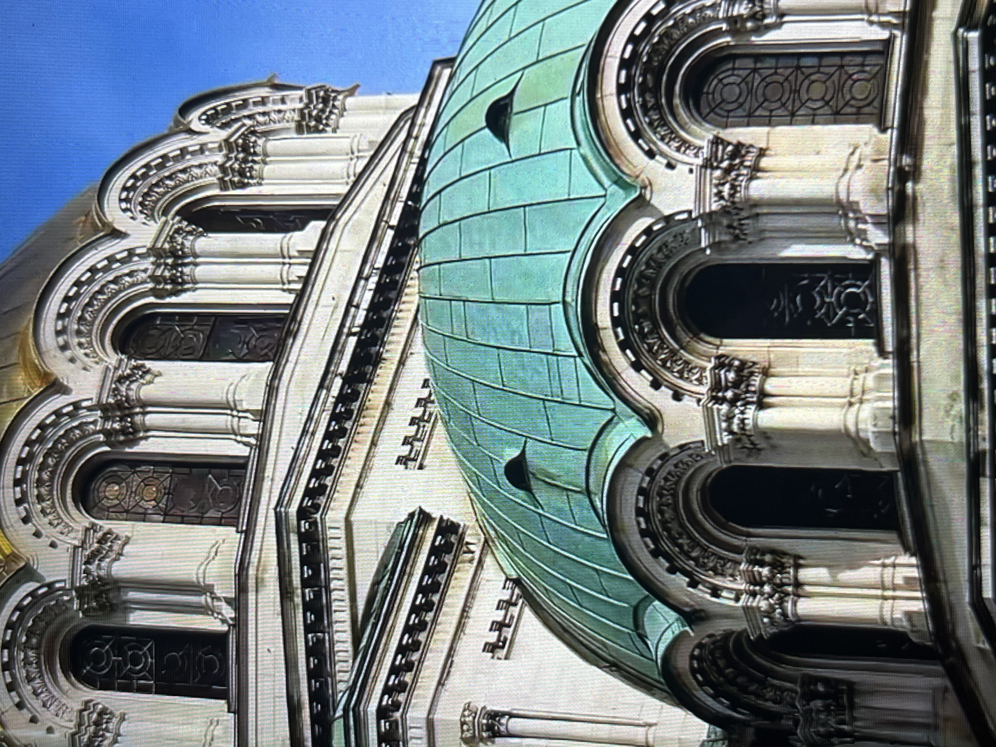 The image shows the exterior architectural details of a building, possibly a church or cathedral, with a prominent green dome. The architectural style features ornate details, arched windows with decorative frames, and what appears to be classical columns or pilasters. The dome is constructed with a pattern of rectangular panels. The sky is visible in the background, indicating that the photograph was taken outdoors. The image does not contain information to confirm the location in the city of Tinaquillo, Venezuela. There are no people visible in the image.
