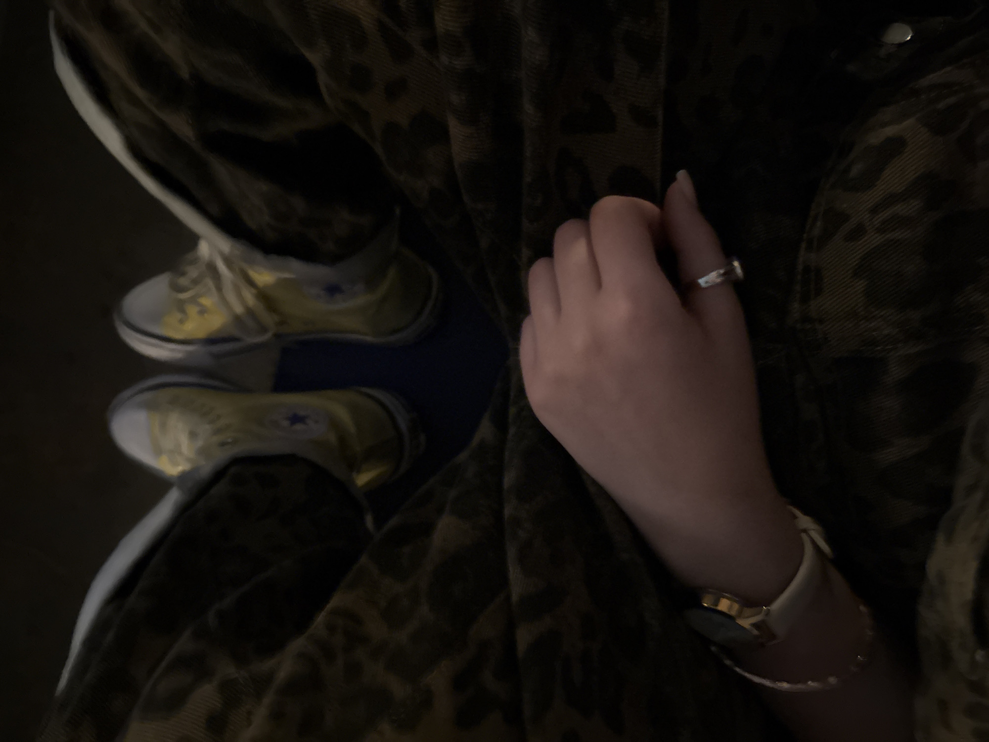 A high-angle shot captures a person seated, wearing yellow Converse sneakers. The subject is wearing patterned pants and shirt. The left hand of the individual is prominently displayed, adorned with a ring and a watch paired with a bracelet on the wrist. No definitive location in Yerevan, Armenia is discernible from the provided image.
