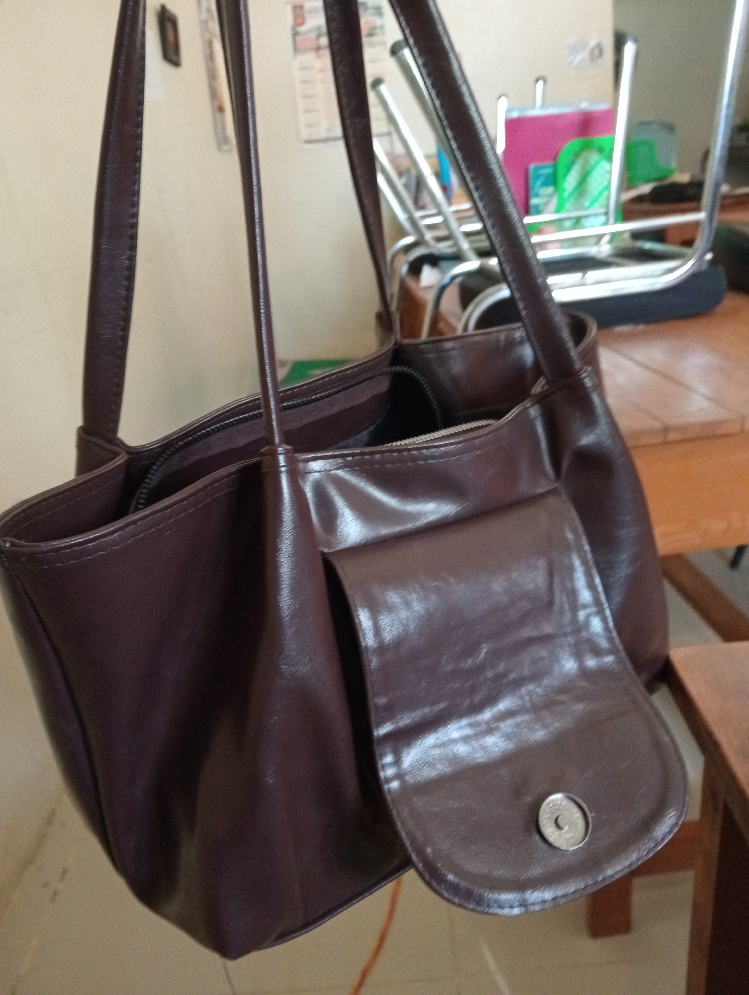 The image shows a dark brown leather handbag with shoulder straps. The bag is open, revealing the interior. A flap with a magnetic closure is visible on the front of the bag. In the background, there are some chairs and a table. There is no specific indication of the location in Wanasalam, Indonesia.
