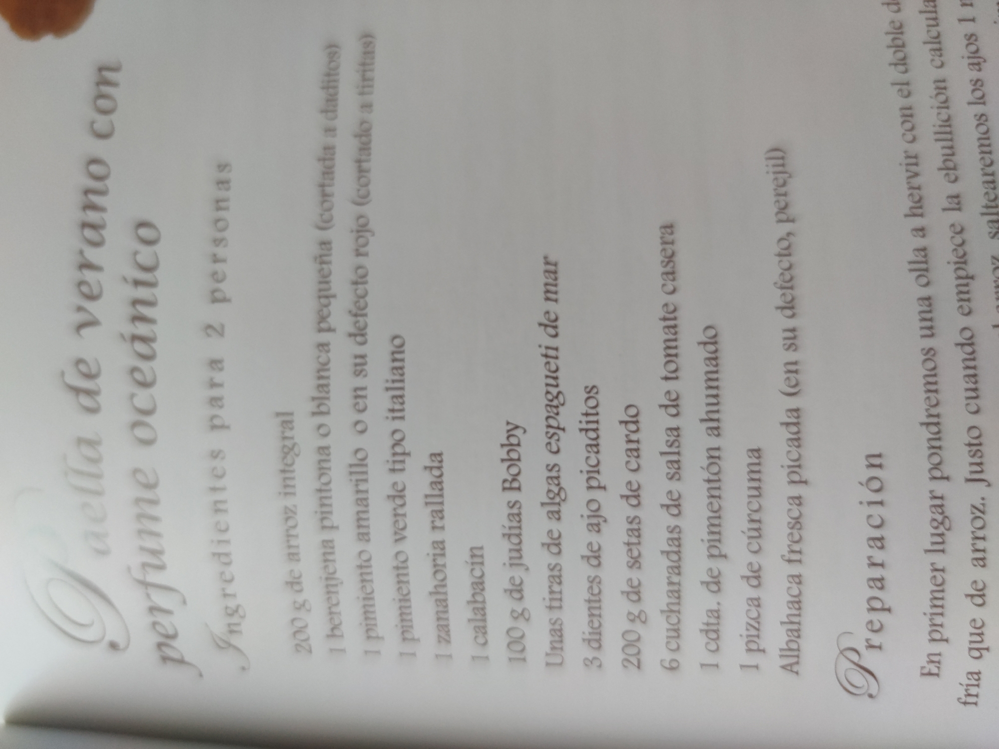 Here is a description of the image:
The image shows a recipe for "Paella de verano con perfume oceánico" (Summer Paella with Ocean Perfume) for 2 people. The recipe is presented in a list format. The ingredients are listed as follows: 200g of brown rice, 1 small spotted or white eggplant (diced), 1 yellow or red bell pepper (cut into strips), 1 Italian green pepper, 1 grated carrot, 1 zucchini, 100g of Bobby beans, some strips of sea spaghetti seaweed, 3 minced garlic cloves, 200g of cardo mushrooms, 6 tablespoons of homemade tomato sauce, 1 teaspoon of smoked paprika, 1 pinch of turmeric, and fresh chopped basil (or parsley). The section labeled "Preparación" (Preparation) starts by stating that you should boil water in a pot with twice the amount of rice.