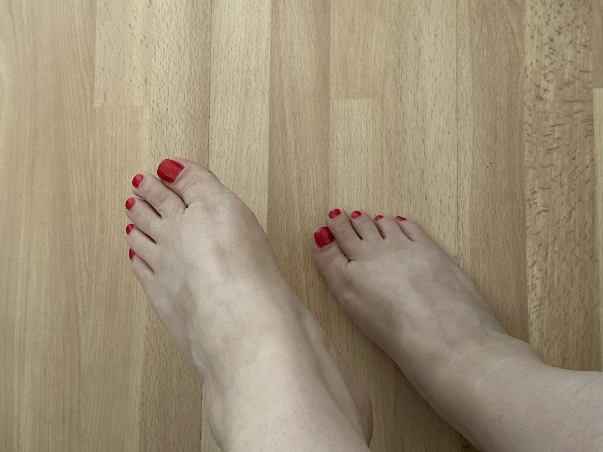 Two human feet, with toenails painted red, are positioned on a light-colored wooden floor. The feet are viewed from a top-down perspective, with the toes of both feet facing towards the upper right of the frame. The lighting suggests an indoor environment. There is no discernible indication of a specific location within the city of Krefeld, Germany.