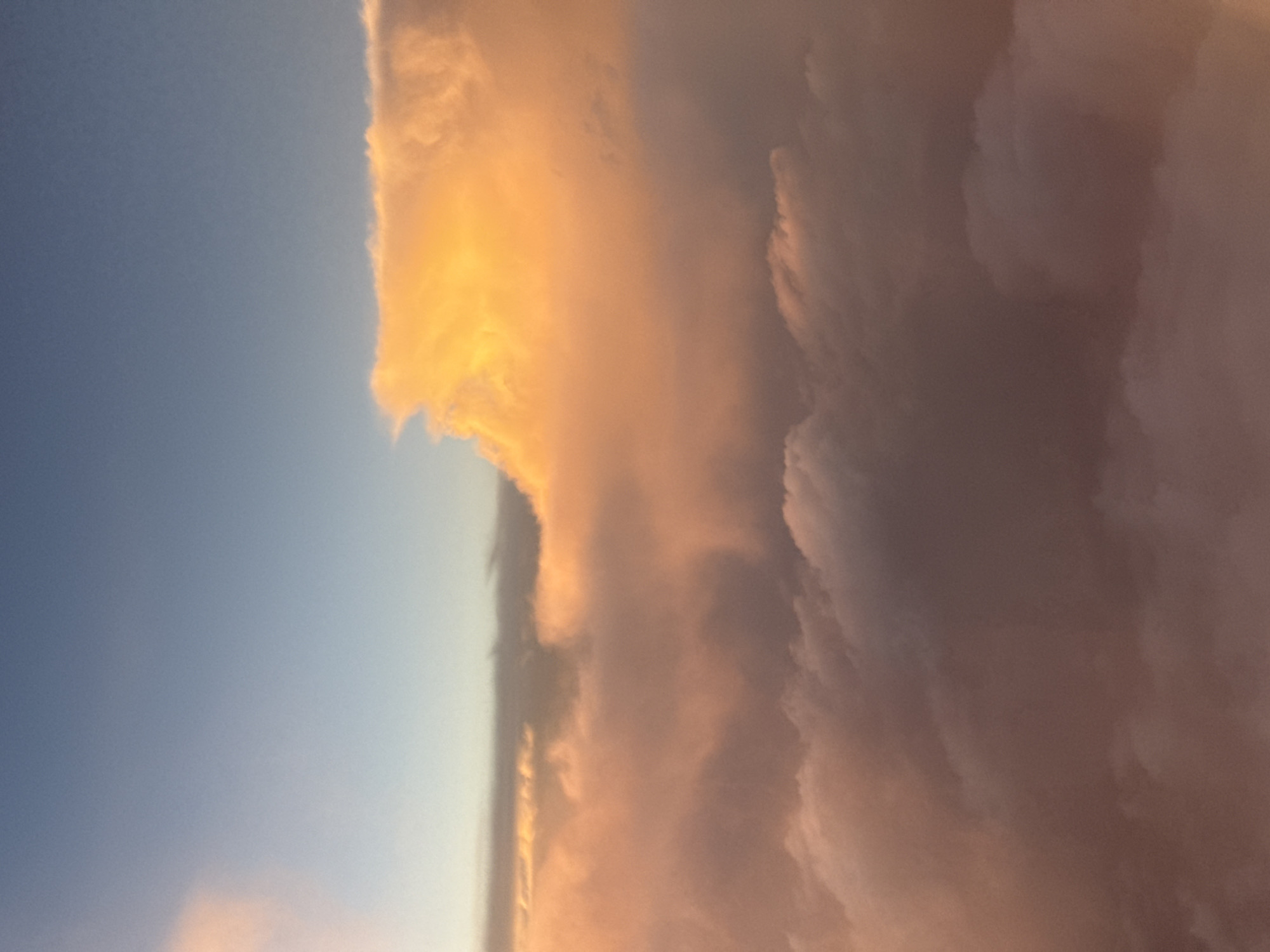 The image shows a view of the sky with clouds at sunset or sunrise. The sky is blue on the left, and the clouds are illuminated with a warm, orange light, possibly from the sun. The right side of the image is dominated by dense, dark clouds. There is no verifiable evidence within the picture to pinpoint the location as Mexico City, Mexico. There are no discernible people, subjects, or objects, so there are no actions or interactions taking place.