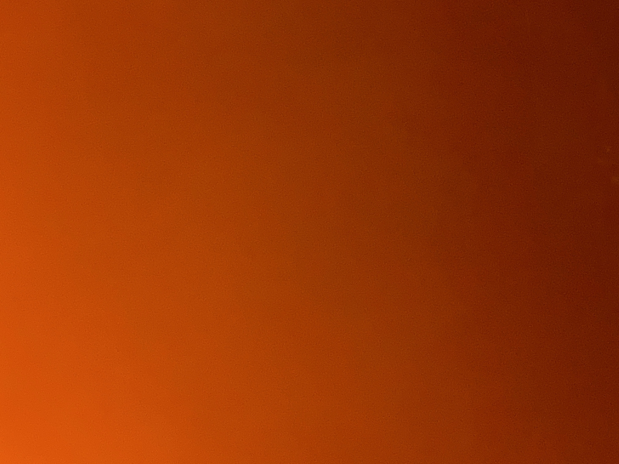 The image is a close-up, full-frame shot of a textured, uniform surface. The color is a gradient of orange and dark red, with the lighter orange at the top and transitioning to a deeper red at the bottom. The texture appears to be fine-grained and consistent throughout, resembling a painted wall or fabric. There are no discernible objects, people, or actions visible in the image. The location in Haines Junction, Canada, is not ascertainable from the visual information presented.