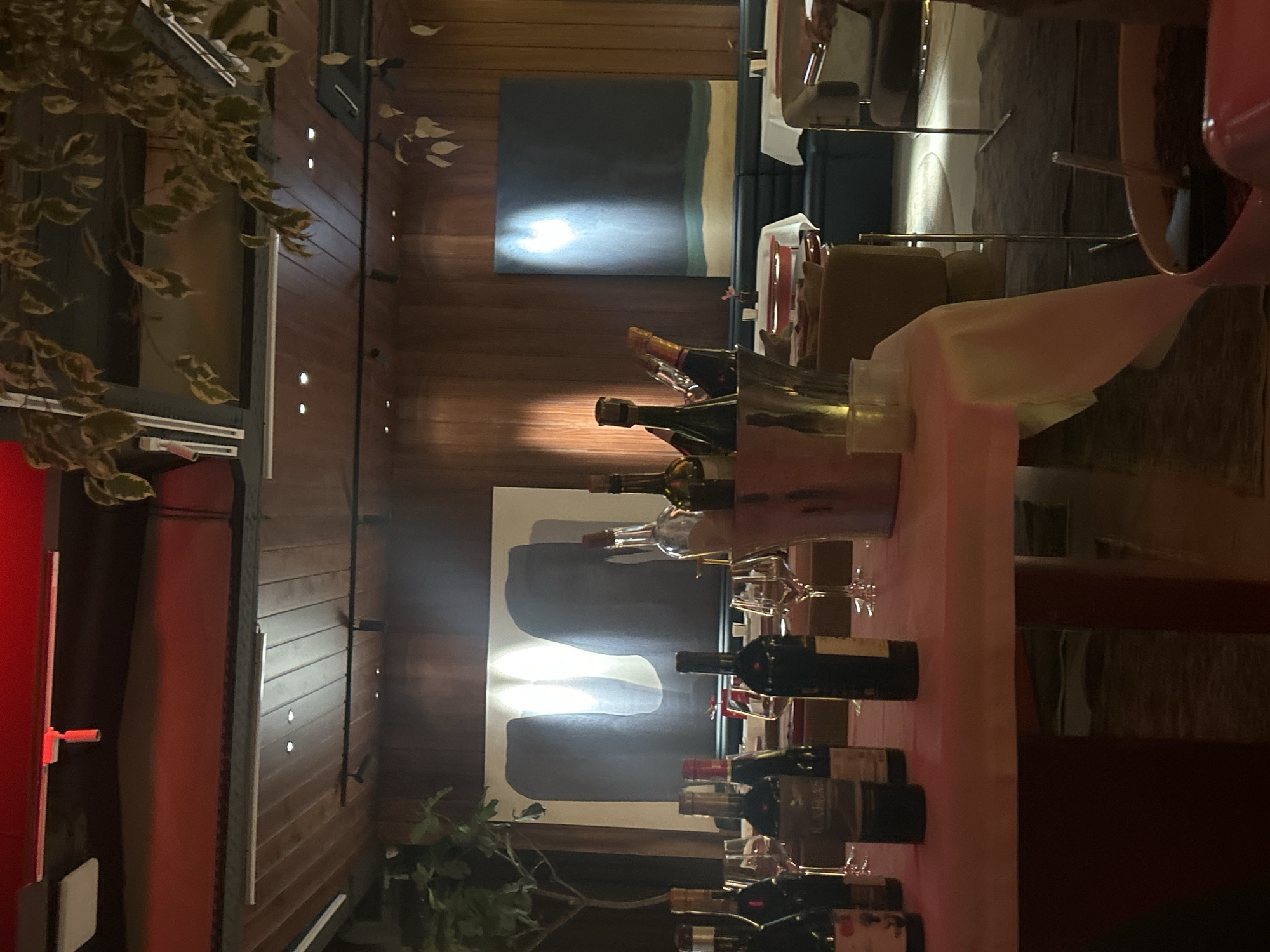 The image depicts a dining area, possibly in a restaurant, featuring a table set with wine bottles and glasses. A painting adorns the wall, while plants add a touch of greenery to the scene. Yerevan, Armenia, is not directly discernible from this image.