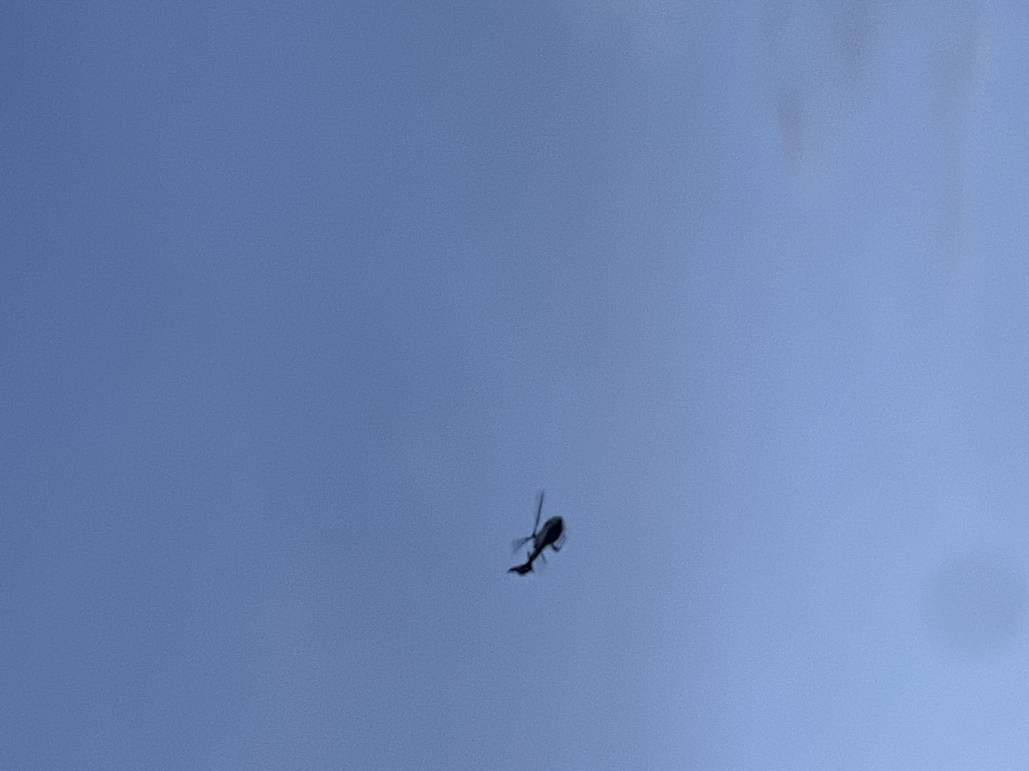 A helicopter is in flight against a clear blue sky. The location is Unknown, Unknown.