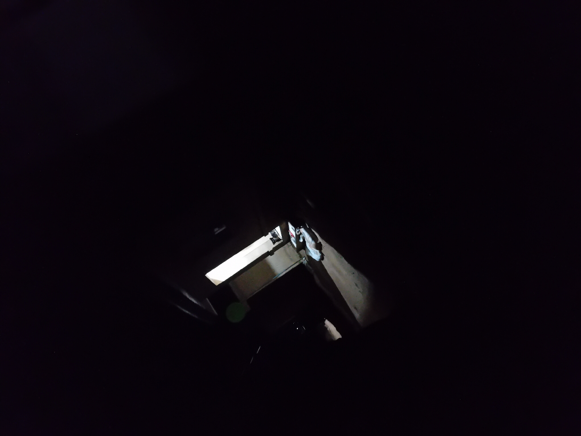 The image depicts a dark, possibly abandoned, interior space. A doorway is visible, illuminated from beyond, suggesting a passage to another area. In the foreground, there are several objects lying on the ground, appearing to be fabric or possibly discarded clothing. The overall impression is one of neglect and darkness. No specific details about the location in Barakin Angundi, Nigeria are provided by the visual information in the image itself.