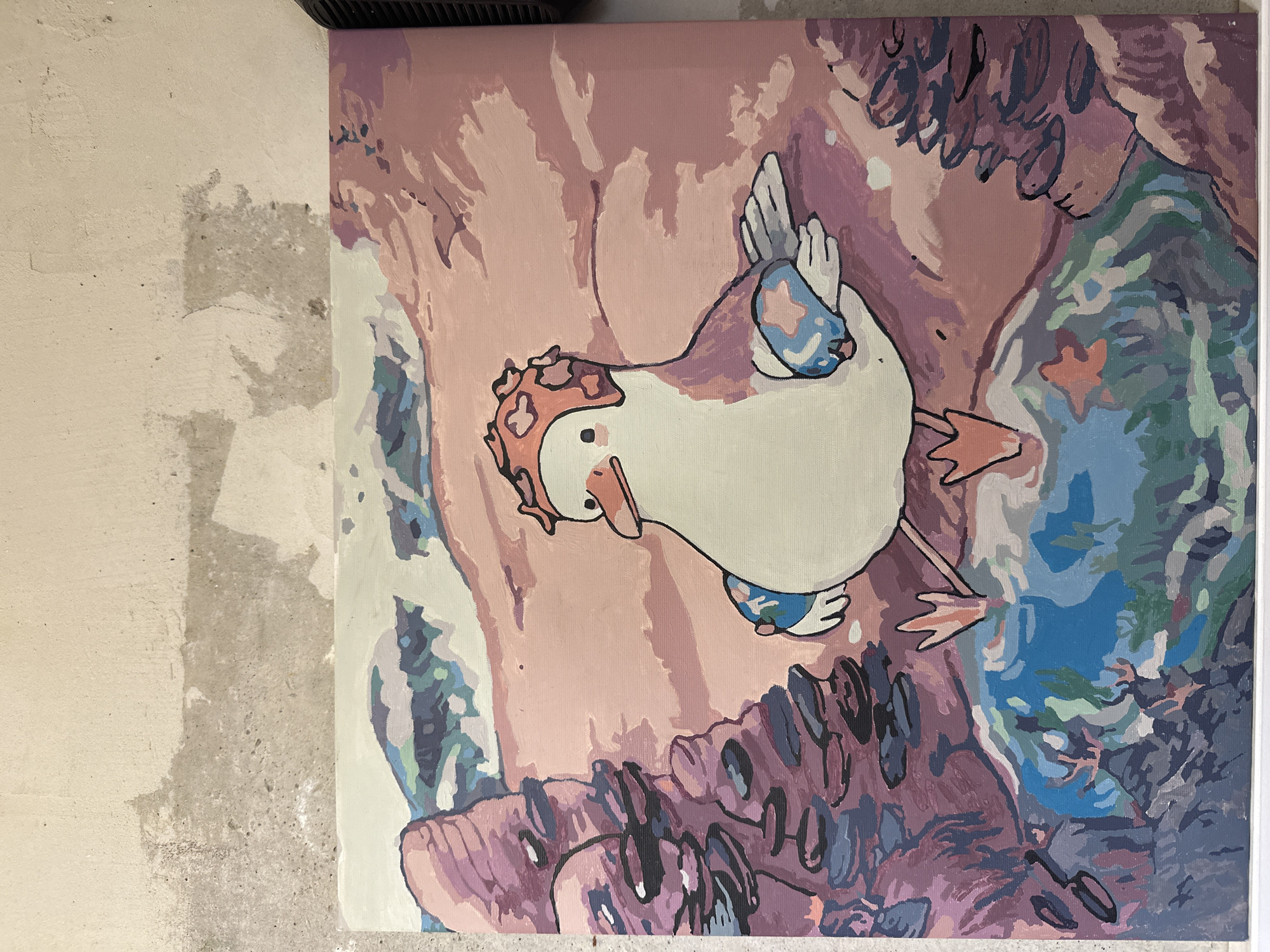 An image displays a vertically oriented canvas painting leaning against an unadorned wall. The painting features a cartoon-like bird, resembling a duck or goose, with a white body, orange beak, and small black eyes. The bird wears a pink and orange patterned headpiece and matching armbands or wing decorations. It appears to be walking or standing within a stylized, abstract landscape.
The background of the painting is composed of distinct blocks of color, primarily shades of pink, purple, blue, and green, with dark outlines separating the areas, giving it a "paint-by-number" aesthetic. These colors suggest natural elements like rocks, water, or foliage.
To the left of the canvas, a rough, light-colored wall with varying textures and darker gray patches is visible. A dark, possibly black, object is partially visible at the top right edge of the canvas, which might be part of a frame or a hanging mechanism. The lighting is even, suggesting an indoor setting. There is no visible text in the image.