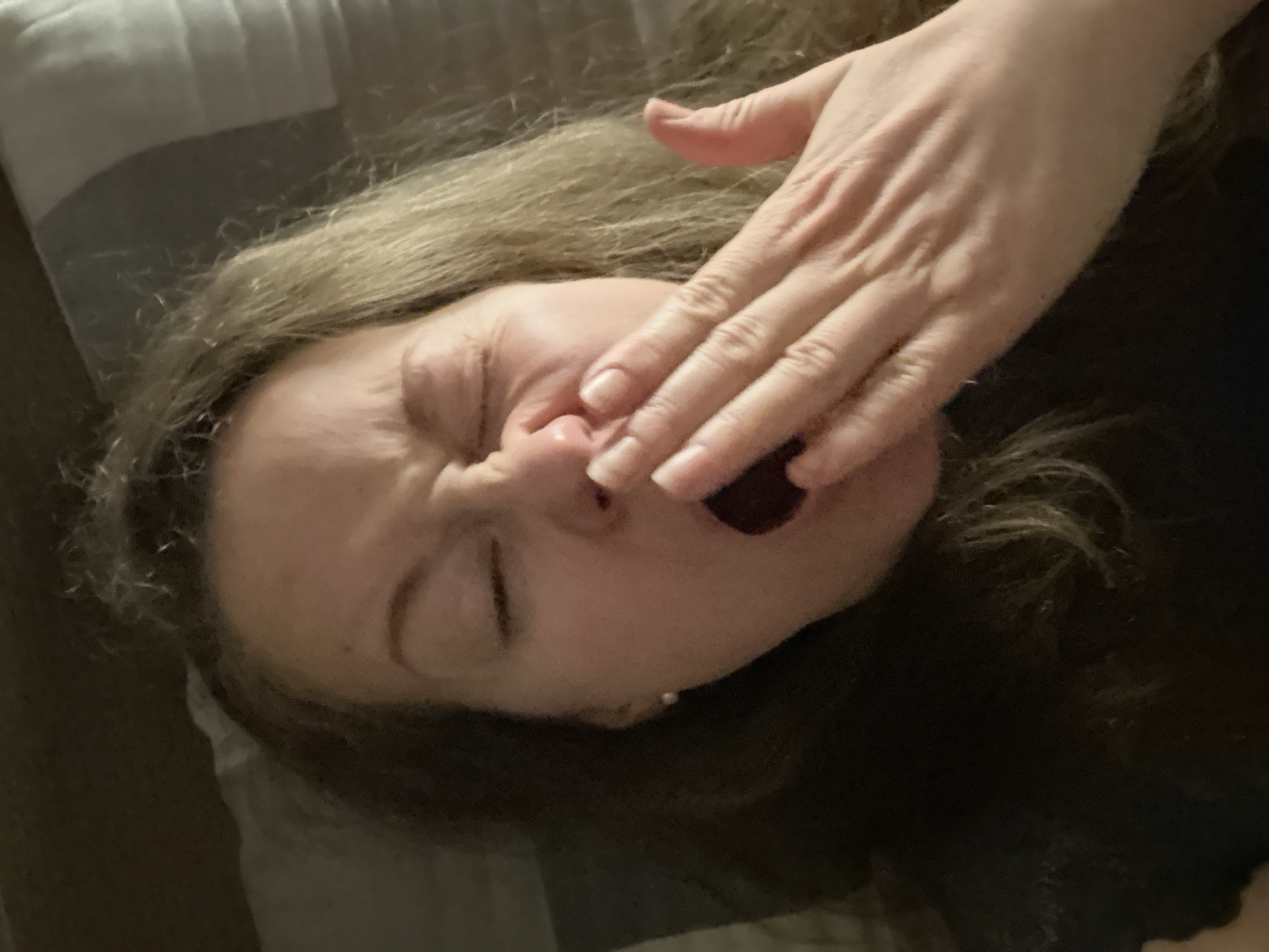 A woman is lying on a gray pillow. Her hair is blonde and dark brown. She is covering her mouth with her hand. Her eyes are closed. The background is dark.
There is no indication of the location in the city of Moscow, Russia.