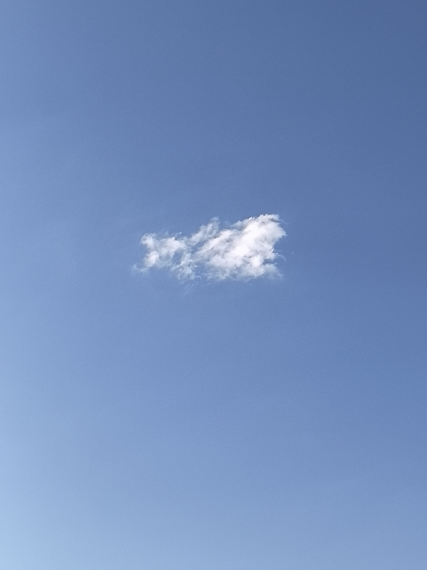 A lone, wispy white cloud drifts across a clear, bright blue sky. The cloud is small and appears to be in a state of formation or dissipation, with some parts denser than others. There are no visible landmarks or signs of human activity in the frame, suggesting an open, unobstructed view of the sky. The image was taken in Bol'shiye Saly, Russia.