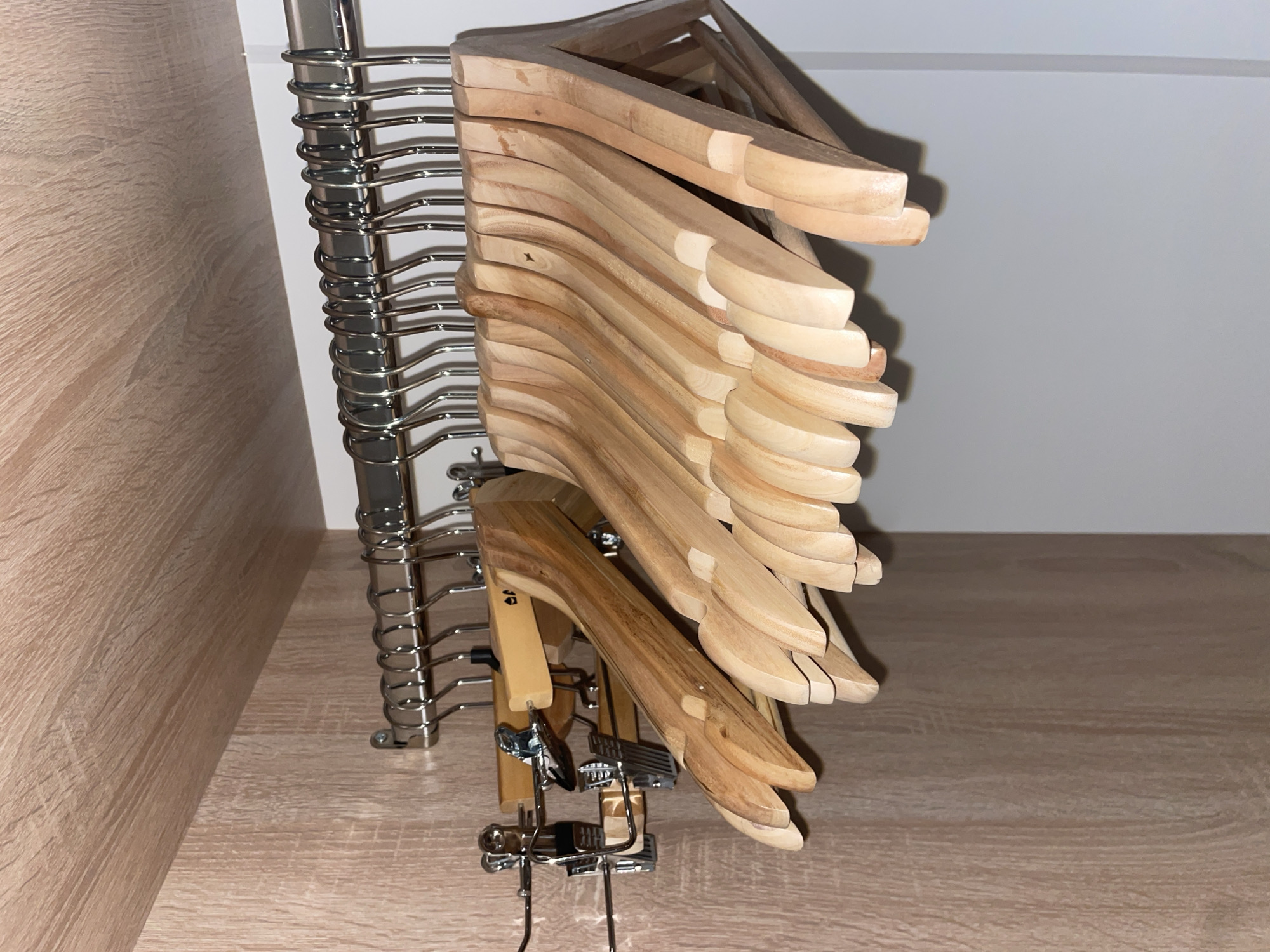 The image depicts the inside of a closet in Poroshkino, Russia. A metal rod runs horizontally across the top, supporting a row of metal hangers. Below these, a collection of wooden hangers, some with clips, are suspended. The closet walls are made of light-colored wood.