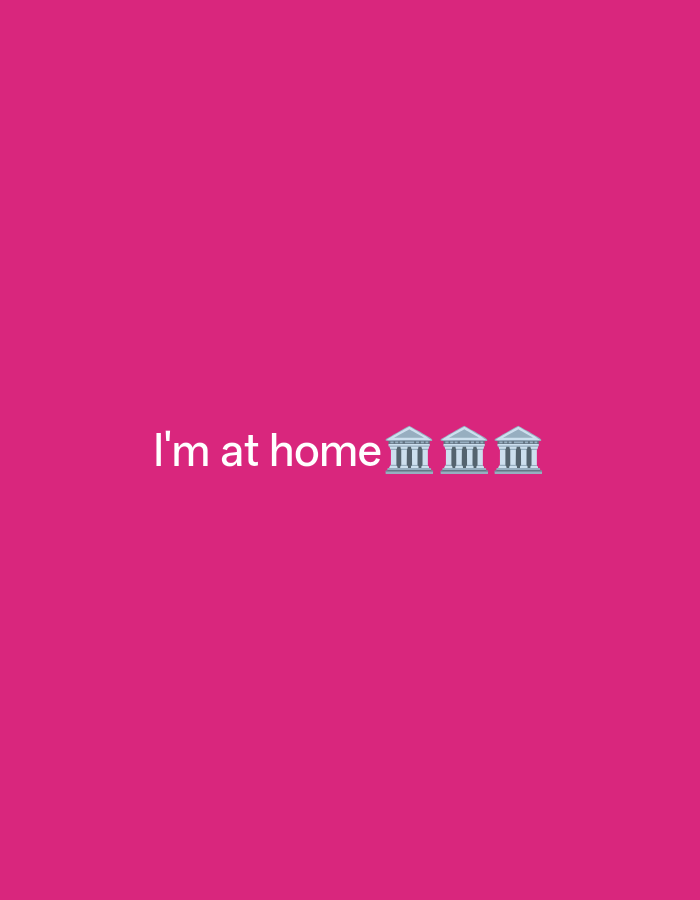 The image is a plain, vibrant pink background. In the center of the image, white text reads "i'm at home" followed by three building emojis, each resembling a classical Greek temple with columns. The text and emojis are positioned horizontally across the middle of the frame. There is no discernible location in the city of Payagaboh, Indonesia, or any other environmental details present. The image is purely graphic design with text and emojis.