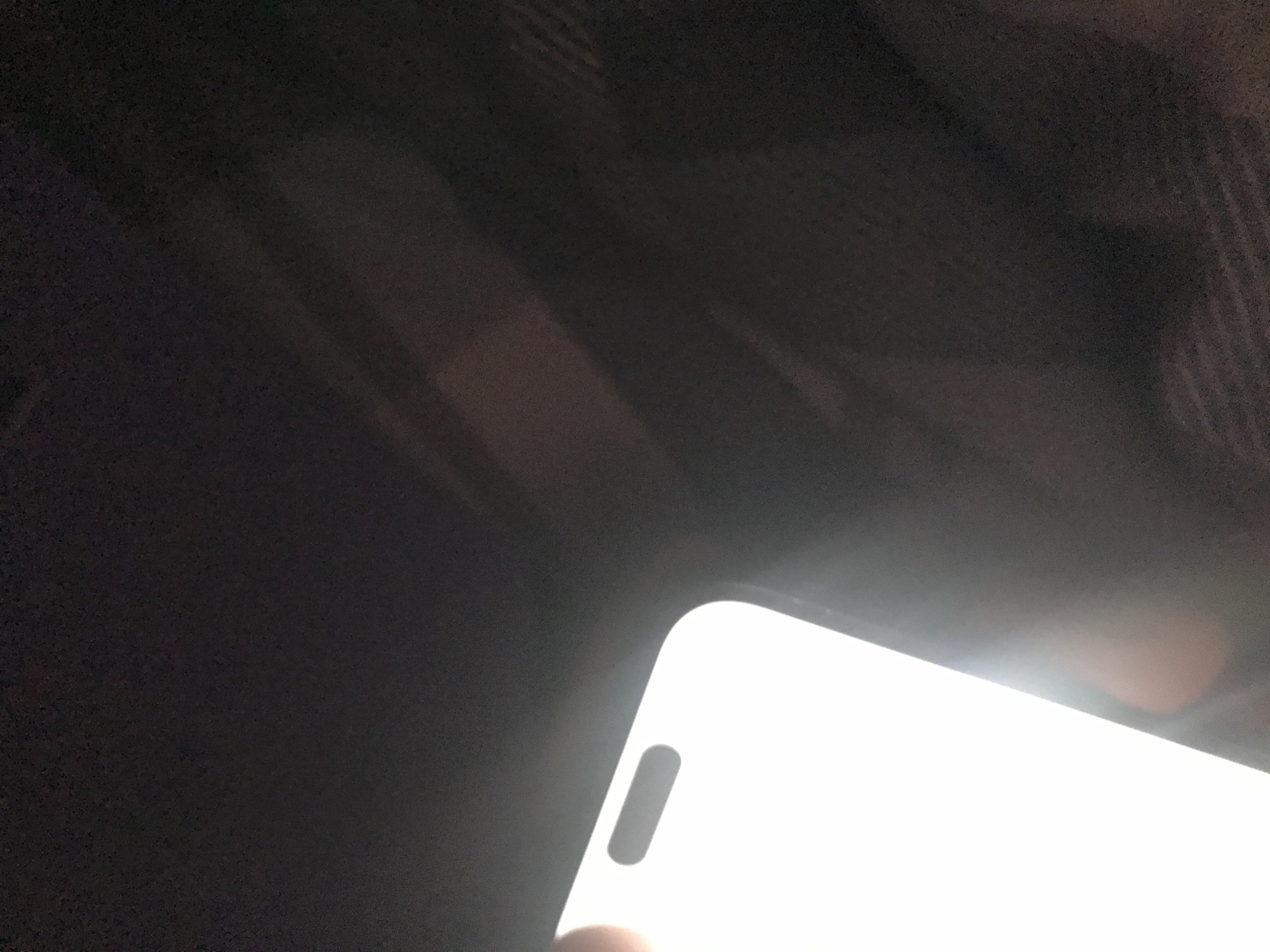 The image shows the corner of a bright white smartphone against a dark, out-of-focus background. The phone has a rounded corner and a small, pill-shaped cutout near the edge. The background appears to be a dark, textured surface. There is no information available to connect the image to Yerevan, Armenia.