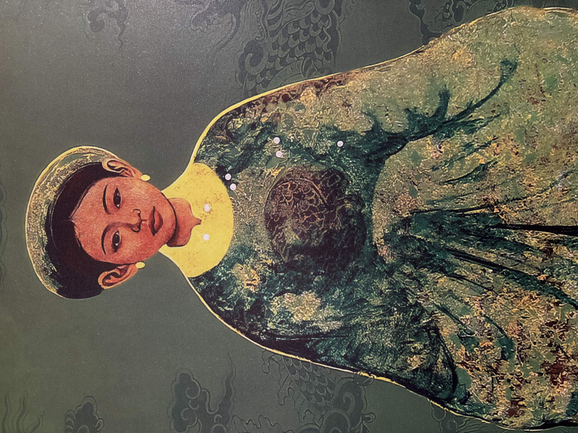 The image depicts a reproduction or artistic rendering of a Vietnamese woman, likely from the Nguyễn Dynasty period, based on her attire. She wears a traditional gown, primarily green with gold and darker green embellishments. The collar of her garment is yellow, and she is adorned with a few small, white beads or pearls on her chest. Her headdress is a dark color with a thin gold trim. Her skin tone is reddish-brown, and she has dark eyes and hair.
The background is a dark green with a subtle floral pattern. The overall image appears to be a painting or a print on textured material, possibly canvas.
While it is difficult to definitively state its exact location within Hà Nội, Vietnam, the image could be found in cultural institutions like the Vietnam National Museum of History or the Vietnam Fine Arts Museum or in art galleries or shops selling traditional Vietnamese artwork.