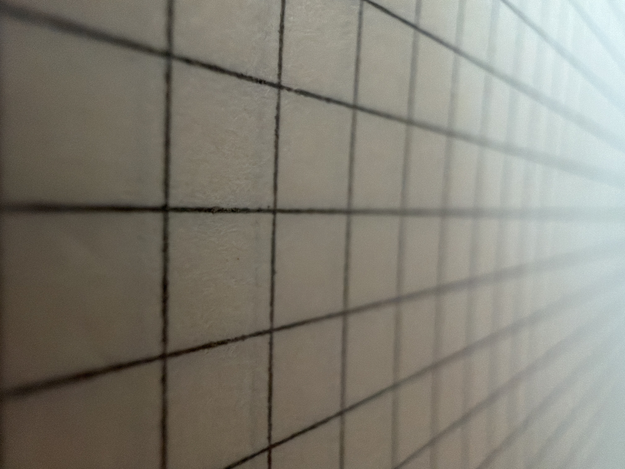 The image is a close-up, low-angle, slightly blurry photograph of a graph paper surface. The graph lines, in dark ink, form a grid that recedes into the distance, creating a sense of perspective. The paper appears to be off-white or light beige, and the lighting is soft, with a gradient from a brighter, lighter tone at the top to a slightly darker tone at the bottom. The texture of the paper is visible, with a subtle graininess. There are no people, objects, or discernible environmental features other than the graph paper itself. The image does not contain any information that would allow for its location to be identified in Kazan, Russia, or any other specific city.
