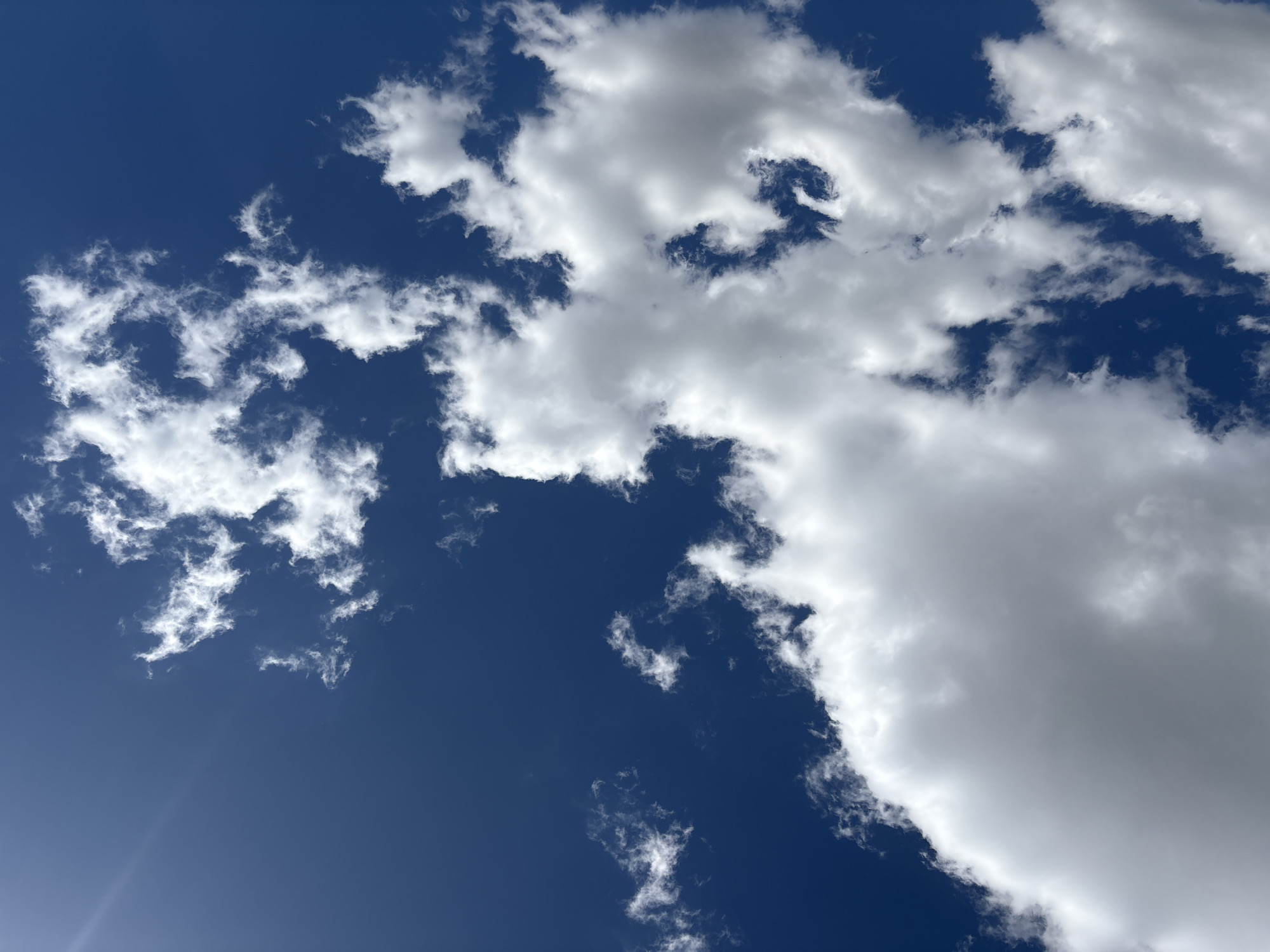 The image shows a bright blue sky with scattered white clouds. There is a bright sun flare in the upper right corner of the image. The image does not contain any information about the city of Pilsen, Czechia, or any people, subjects, objects, or actions.