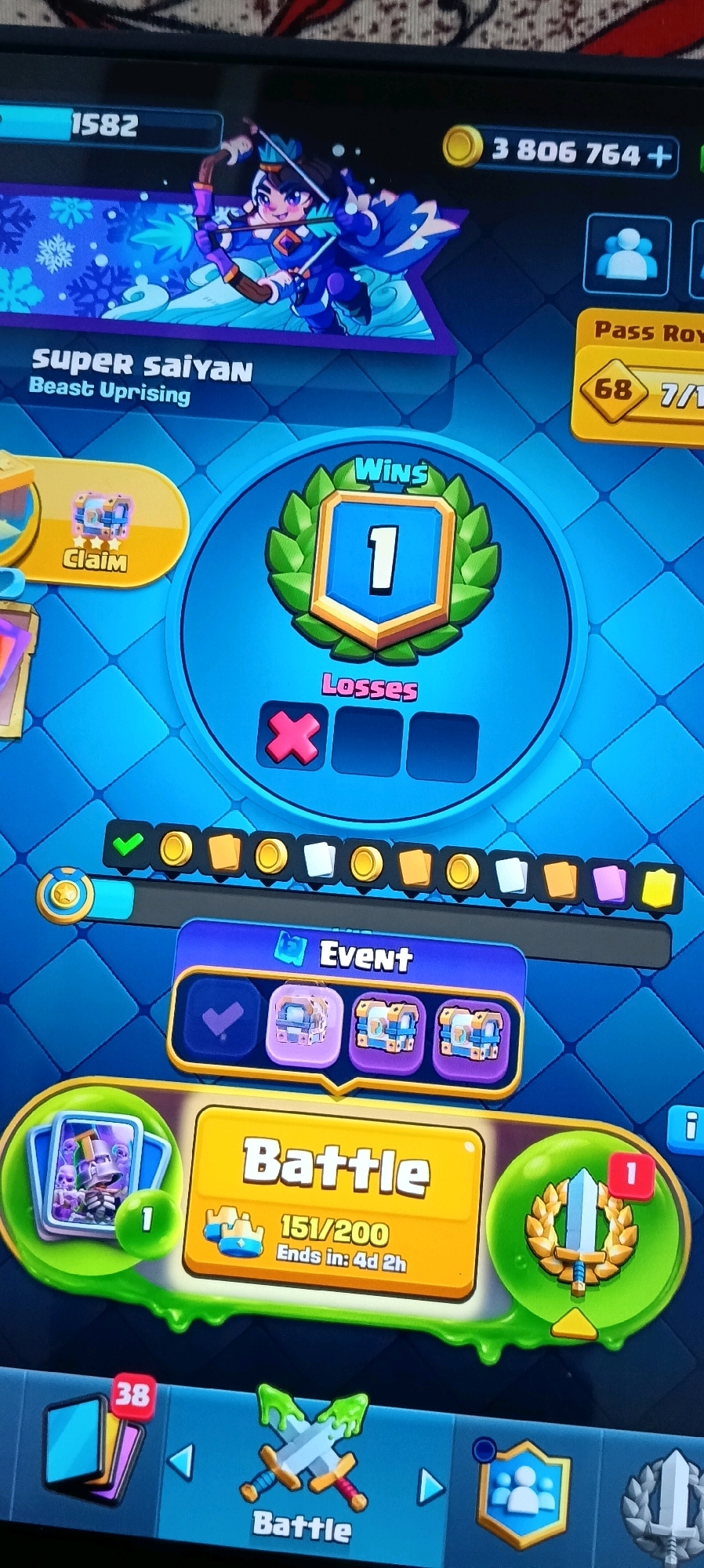 The image shows a screenshot of a mobile game, likely Clash Royale, displayed on a device. The user's in-game name is "Super Saiyan Beast Uprising". The player has 1582 trophies and 3,806,764 gold coins. They have 1 win and 0 losses visible. There is a "Claim" button with a chest icon and an "Event" section with several chest icons. The main action button is labeled "Battle", and a timer indicates an event ends in "4d 2h". Another "Battle" button is present at the bottom of the screen, next to a shield icon with two people on it. The game interface is vibrant and cartoonish, with blue and green as dominant colors. There is no indication of the image being related to Udaipur, India; it is a digital interface on a screen.