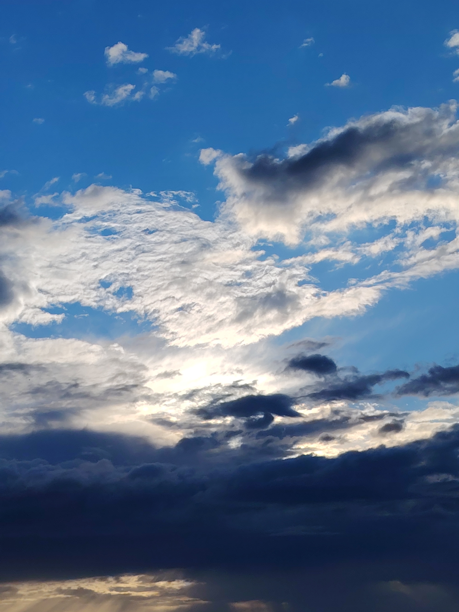 This media file captures a dynamic sky with a variety of clouds. The scene is dominated by the vast expanse of the sky, rendered in hues of bright blue and interspersed with clouds that range from bright white and wispy to dark, ominous grays. The sun is partially obscured by the clouds, creating areas of intense light and shadow. Streaks of sunlight pierce through the lower cloud layers, creating a dramatic effect.
The clouds themselves are varied in texture and form, suggesting a complex weather system. Some are fluffy and scattered, while others appear to be thick, layered formations. The contrast between the bright, sunlit portions of the clouds and the deep, dark shadows is a prominent feature, giving the sky a sense of depth and movement. The overall impression is one of a dramatic and perhaps changing weather condition.
The time of day is likely late afternoon or early evening, given the angle of the sunlight and the intensity of the light filtering through the clouds. The location context provided is Chaikovsky, Russia, though there are no specific visual cues in the image to confirm this. The scene evokes a sense of natural grandeur and can elicit feelings of awe or perhaps anticipation of a weather change. There is no visible text in the image.