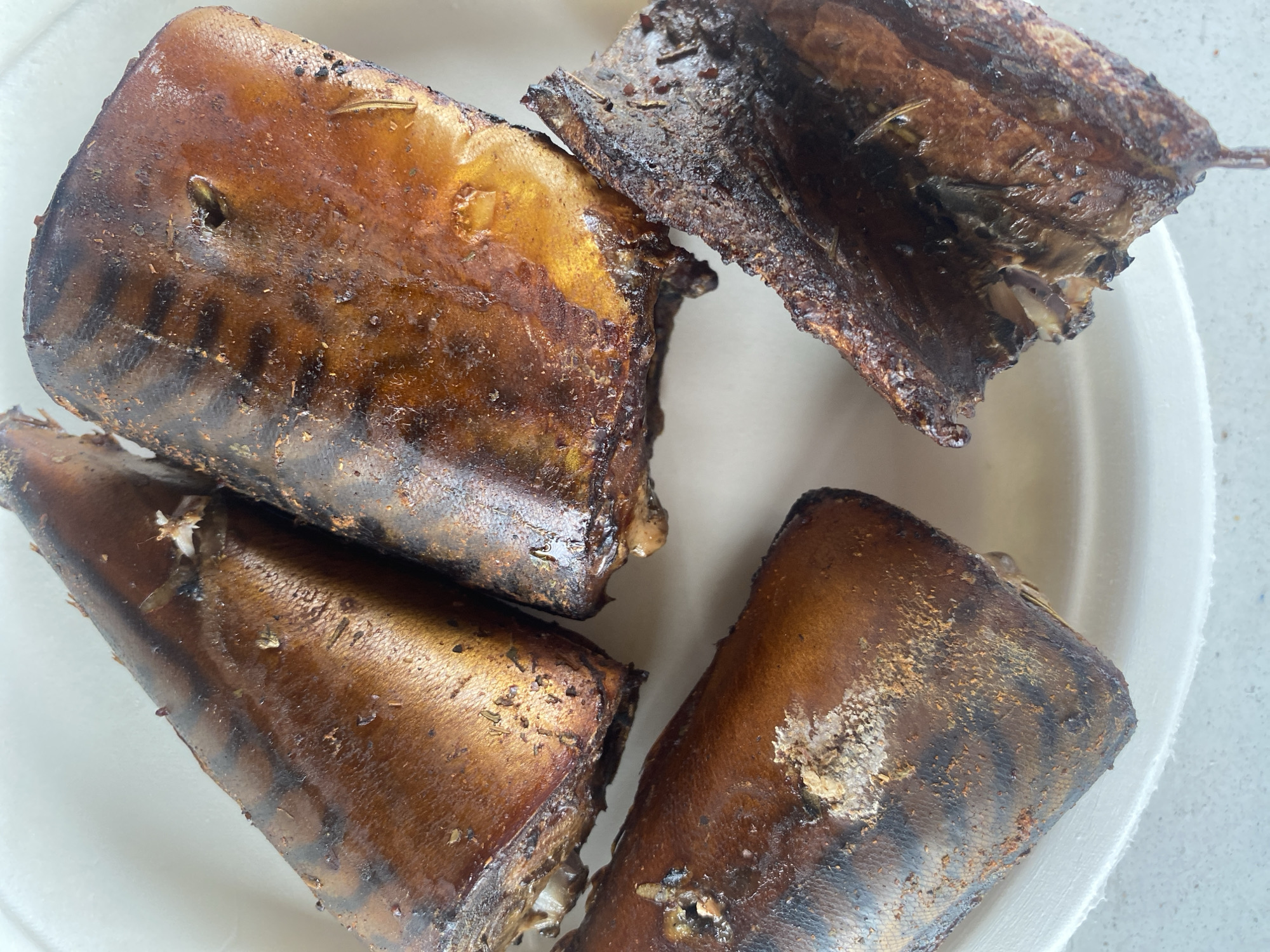 The image shows four pieces of cooked fish on a white surface. The fish is a dark brown color and appears to be oily or glazed. The pieces are arranged in a circular pattern. The image was not taken in Chaikovsky, Russia.