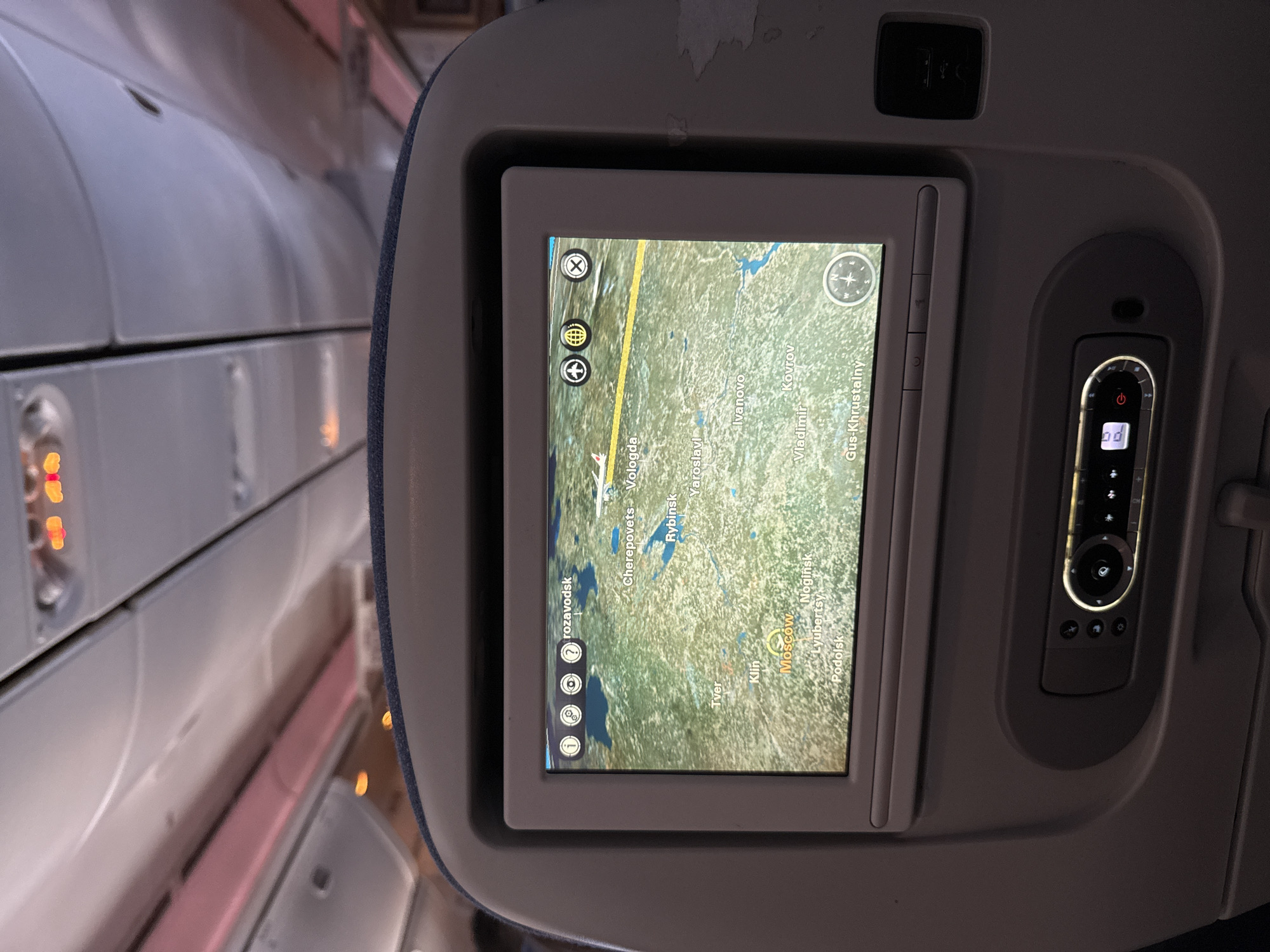 The image shows an airplane in-flight entertainment screen displaying a map of Russia. The map shows various cities including Moscow, Tver, Klin, and Rybinsk, among others. The screen is mounted in the headrest of an airplane seat, with the adjacent airplane cabin visible in the background.