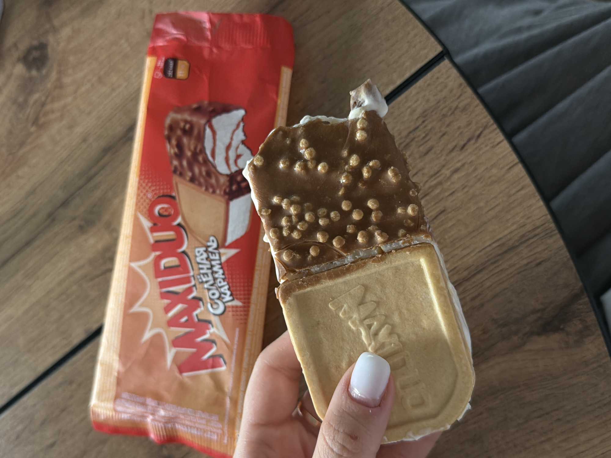 A partially eaten Maxiduo salted caramel ice cream sandwich is held in a person's hand. The wrapper for the ice cream is visible in the background. The location is not specified.