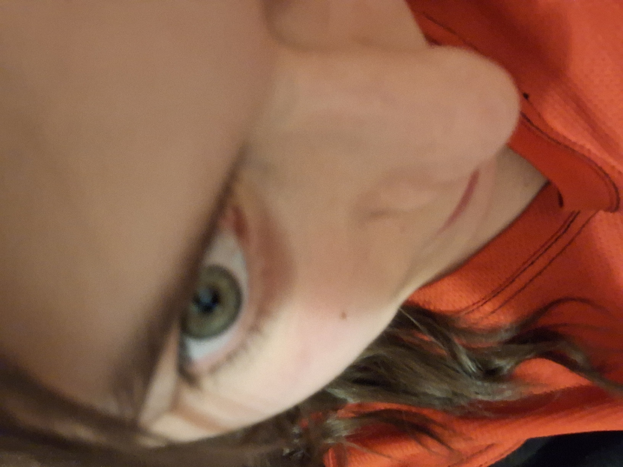 The image shows a close-up, slightly tilted view of a person's face. Visible features include an eye with a green iris, a nose, part of a cheek, and some hair. The person is wearing an orange garment. There is no information available in the image to determine a location, including Panagyurishte, Bulgaria.
