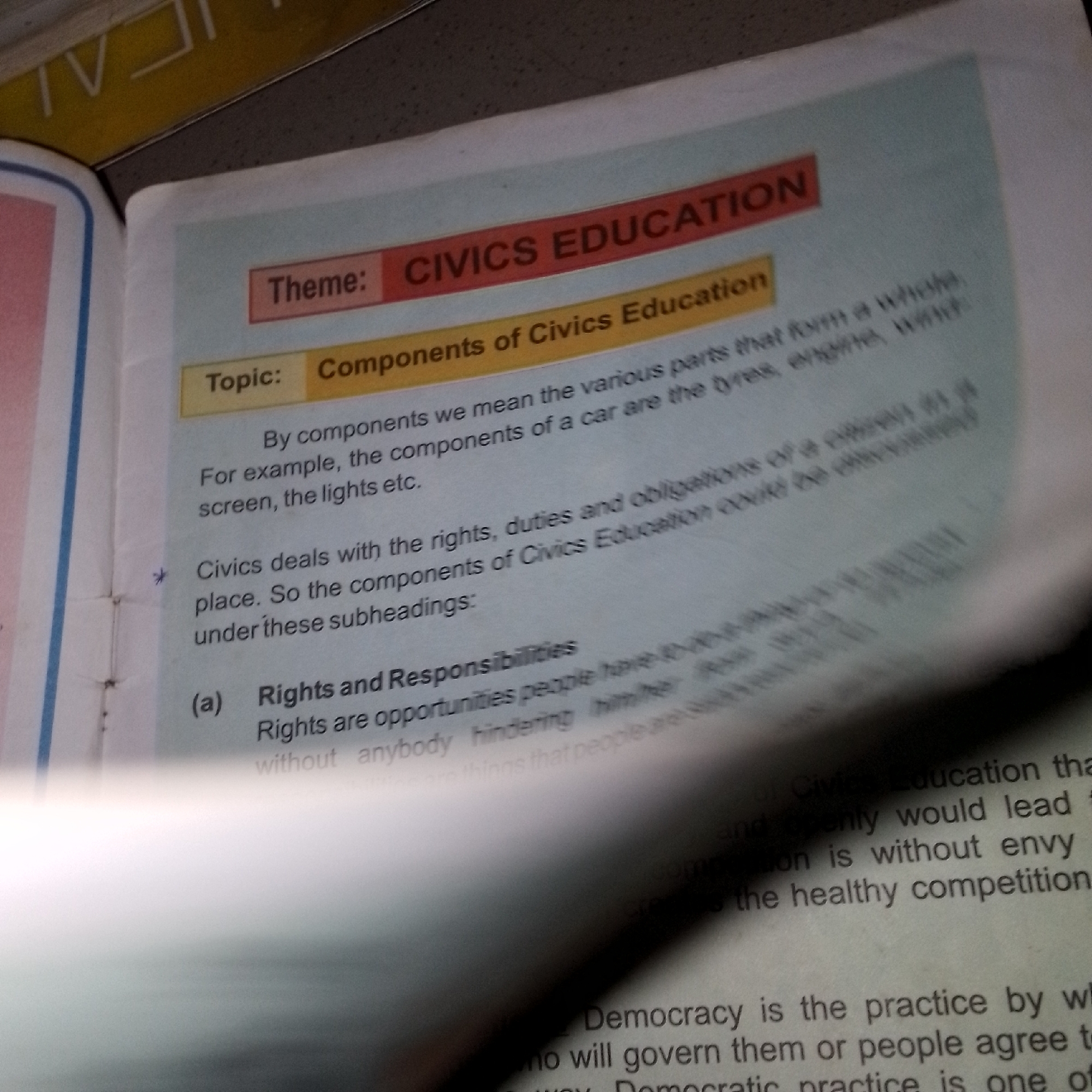 The image shows a close-up view of an open book. The book is titled "CIVICS EDUCATION". The text is printed in English. The book appears to be a textbook or educational material. The pages are white and the text is black. There are some red and yellow headings on the pages. The image is taken from an angle, suggesting the book is lying flat or being held open. There are no people or any environmental elements visible in the image. The location is unknown.