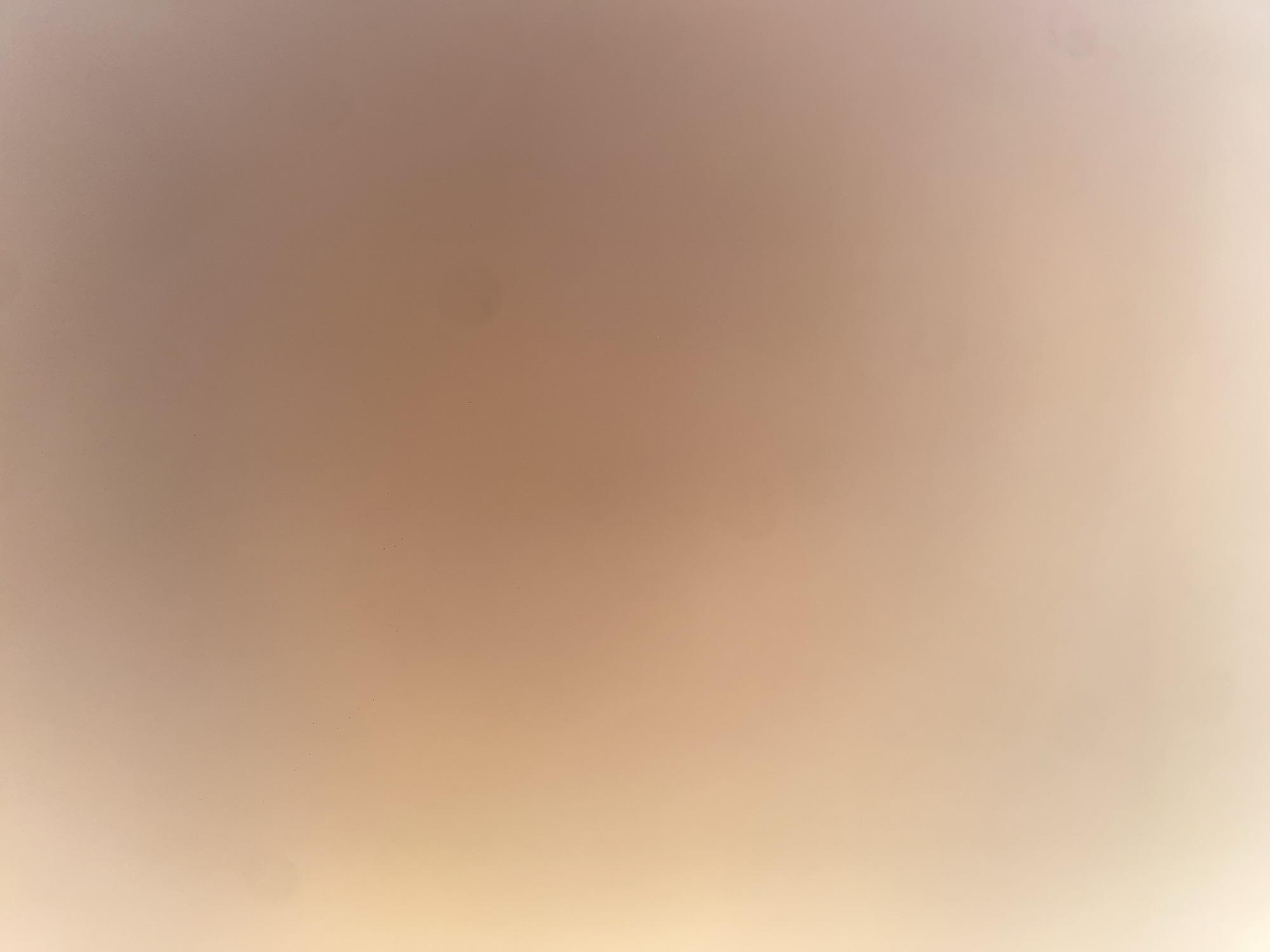 The image is a blurred, abstract photograph with a gradient of warm colors, ranging from light beige on the left to a muted reddish-brown on the right. There are several small, dark specks scattered across the surface. The lighting appears soft and diffused, creating a hazy effect. There are no discernible objects, people, or actions depicted in the image. The location in Ablanitsa, Bulgaria, is not visually represented.