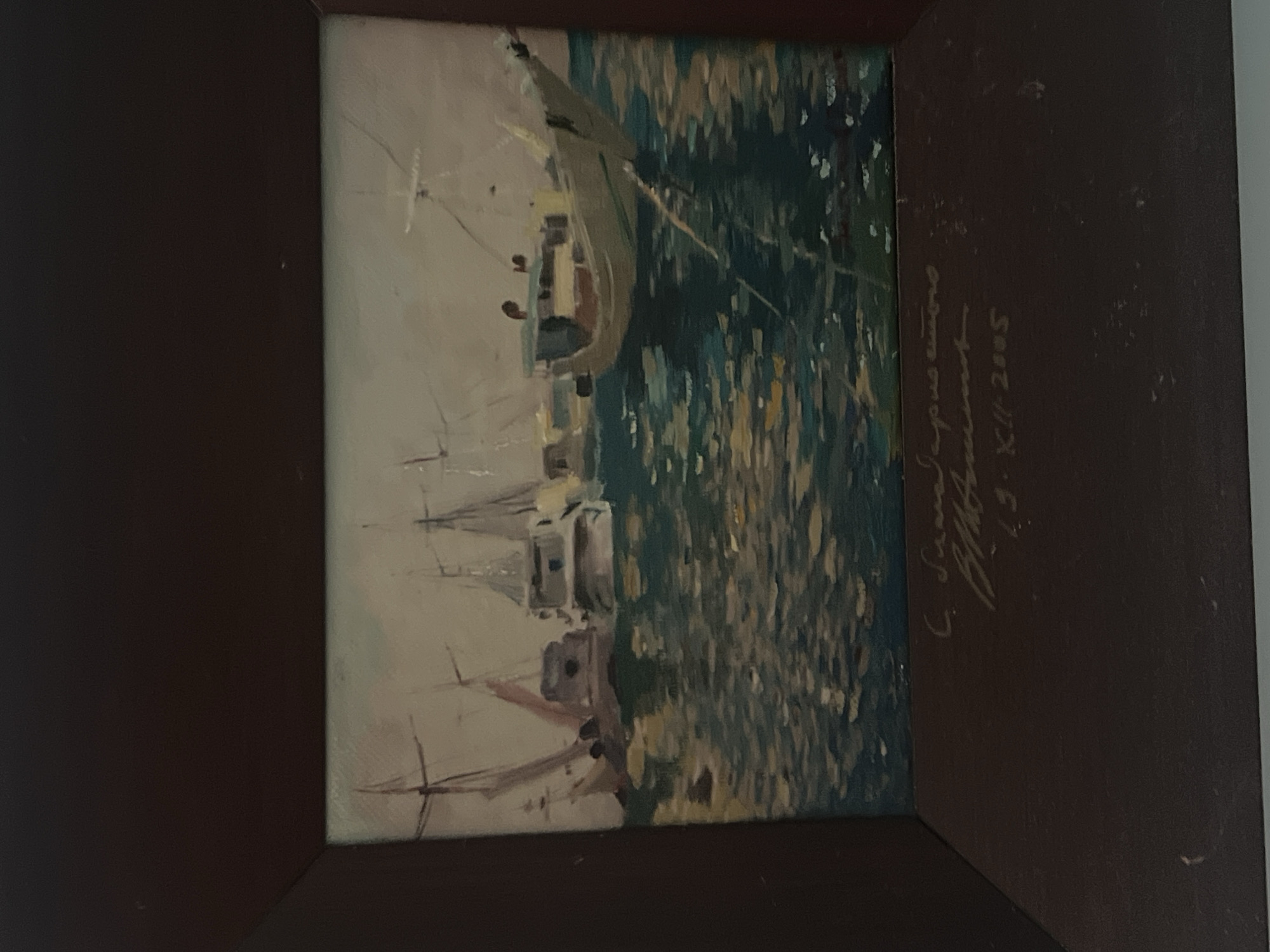 This is a painting of boats in a harbor. The painting is framed in a dark brown frame. The painting itself depicts several boats with masts, floating on water that reflects the sky and boats. The style of painting is impressionistic, with visible brushstrokes. The water is depicted with shades of blue, green, and yellow, suggesting sunlight glinting on the surface. The boats are rendered in muted colors, with details of their structures visible.
Below the painting, there is an inscription in a handwritten script, which appears to be a signature and a date. The script is difficult to read with certainty, but it seems to include Cyrillic characters and the year "2005".
The question asks to include the location in the city of Sochi, Russia. However, there are no visual cues in the painting or the inscription that definitively identify it as being located in Sochi, Russia. The scene depicted is a generic harbor with boats, which could be found in many coastal locations. Without additional information or context, it is impossible to pinpoint the location to Sochi.