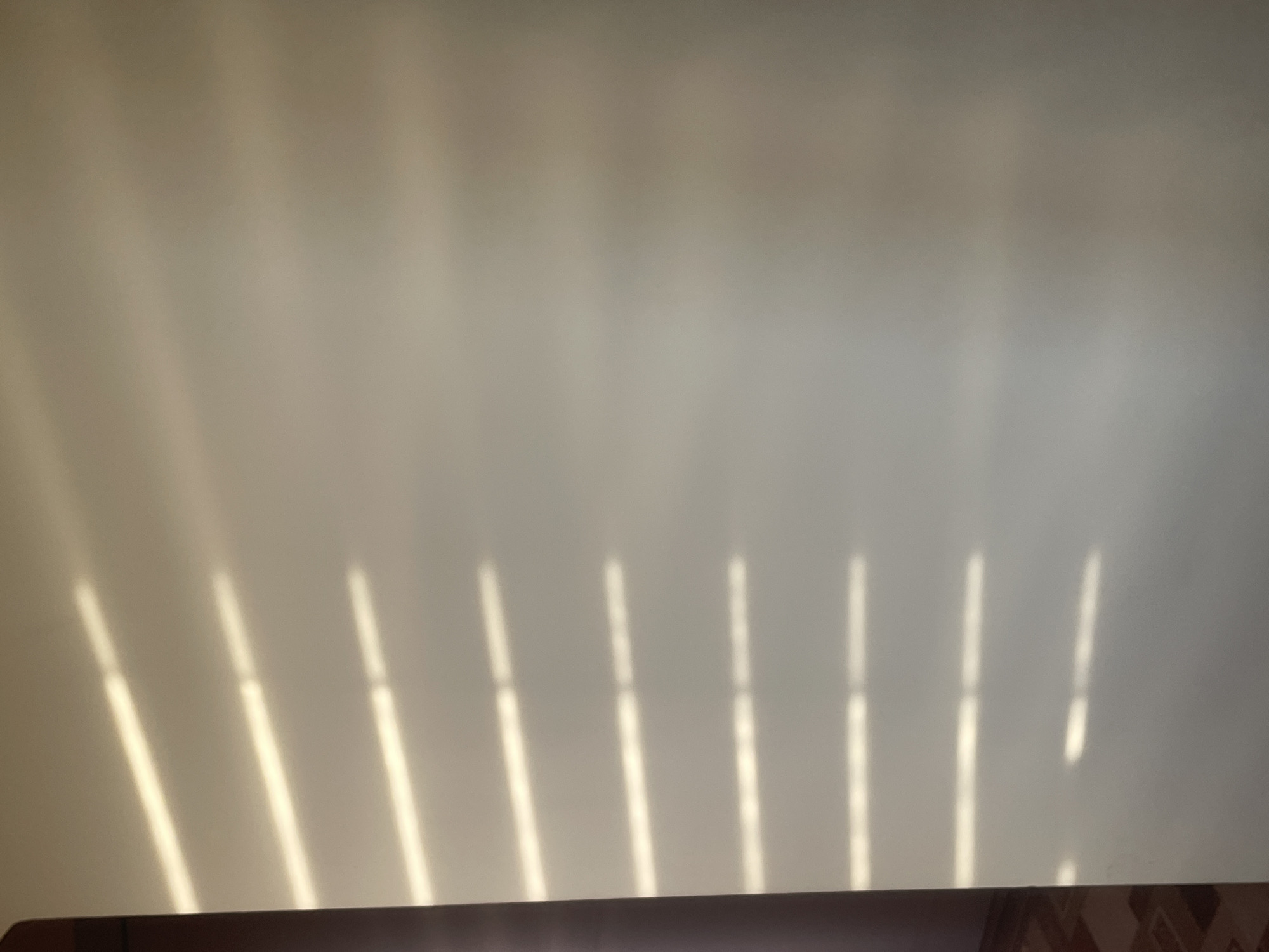 The image shows a close-up of a plain, light-colored wall with horizontal stripes of sunlight casting shadows. The stripes are angled and appear to be formed by blinds or shutters. The lighting suggests it is daytime, and the environment seems to be indoors. There are no people or any other objects visible in the frame. The exact location in Lviv, Ukraine, cannot be determined from this image.