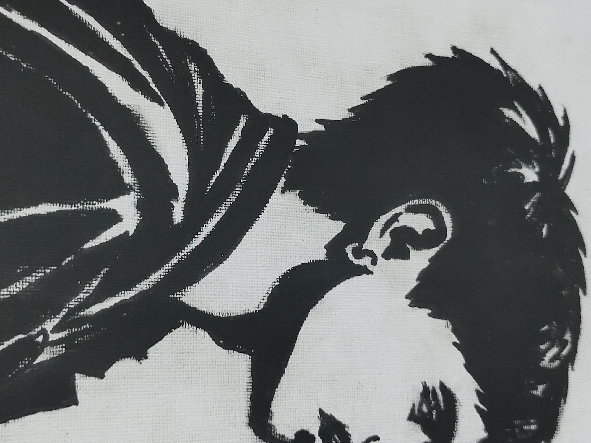 The scene presents a close-up, monochromatic artwork on a textured white surface, likely canvas, depicting a male figure in a high-contrast, black-on-white stencil style. The artwork is located in Davao City, Philippines. The figure is shown from the chest up, in profile, looking downwards and to the right. The subject has short, spiky hair, and an ear is clearly visible. The facial features are rendered as a dark silhouette, suggesting a somber or contemplative expression with a downturned gaze. The upper torso is clad in a garment with visible folds or a hood, indicated by bold black lines around the neck and shoulder area. The weave of the underlying white material is distinctly visible throughout the image, particularly along the edges where the black pigment meets the white background.
