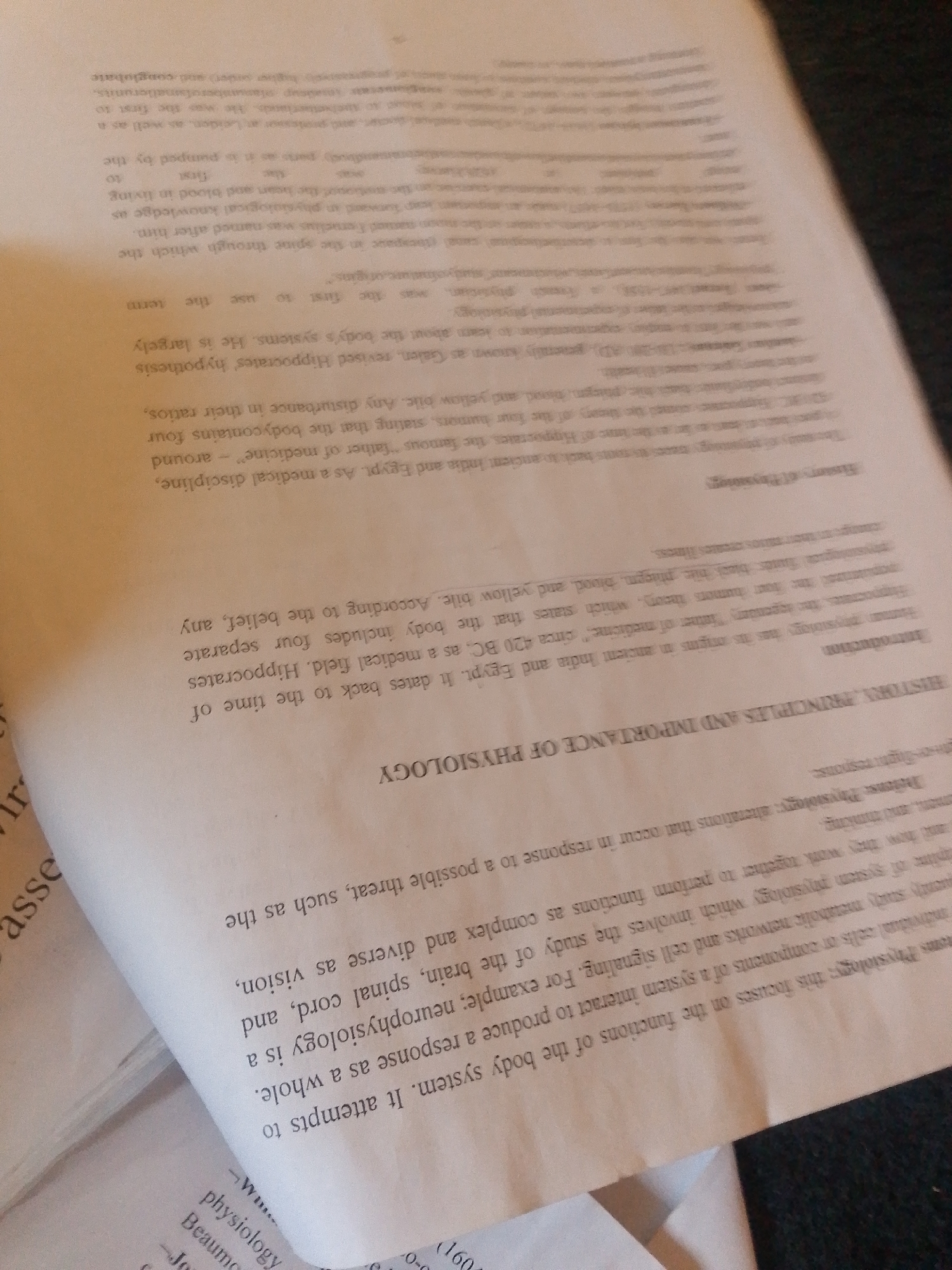 The media file is a close-up, angled shot of an open book, with the text mostly legible. The book appears to be a historical or academic text, with sections titled "HISTORY, PRINCIPLES AND IMPORTANCE OF PHYSIOLOGY" and "Introduction". The content discusses the origins of human physiology, mentioning figures like Hippocrates and Galen, and their theories about the body's humors. The text also touches on neurophysiology and defense physiology. Some lines of text are partially obscured by the curve of the book's pages or are cut off by the frame. The lighting suggests an indoor setting, possibly under artificial light. There are no people or objects other than the book visible in the frame, and no specific details about the time of day, weather, or location cues that can be discerned from the image itself. The overall tone of the text is informative and educational.
